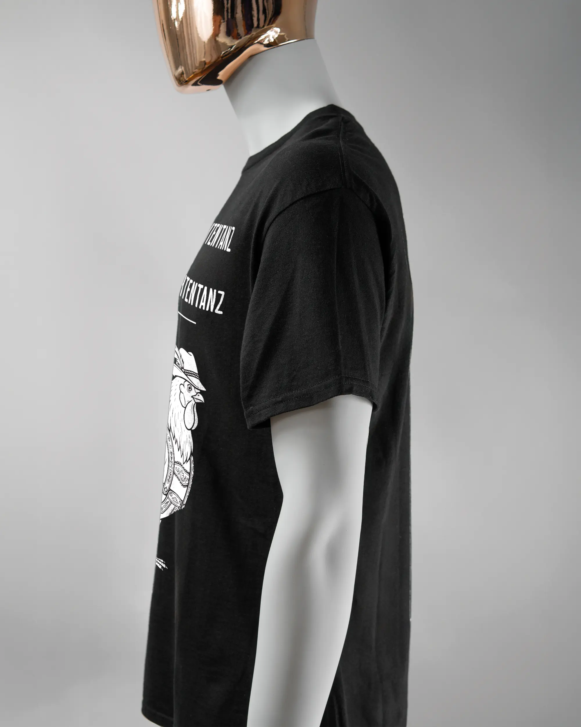 Seitenansicht des Basic Unisex T-Shirt Regular von Maondo mit dem Design Trachtentanz vorne in der Farbe Black und in der Größe L getragen von einer maskulinen Puppe