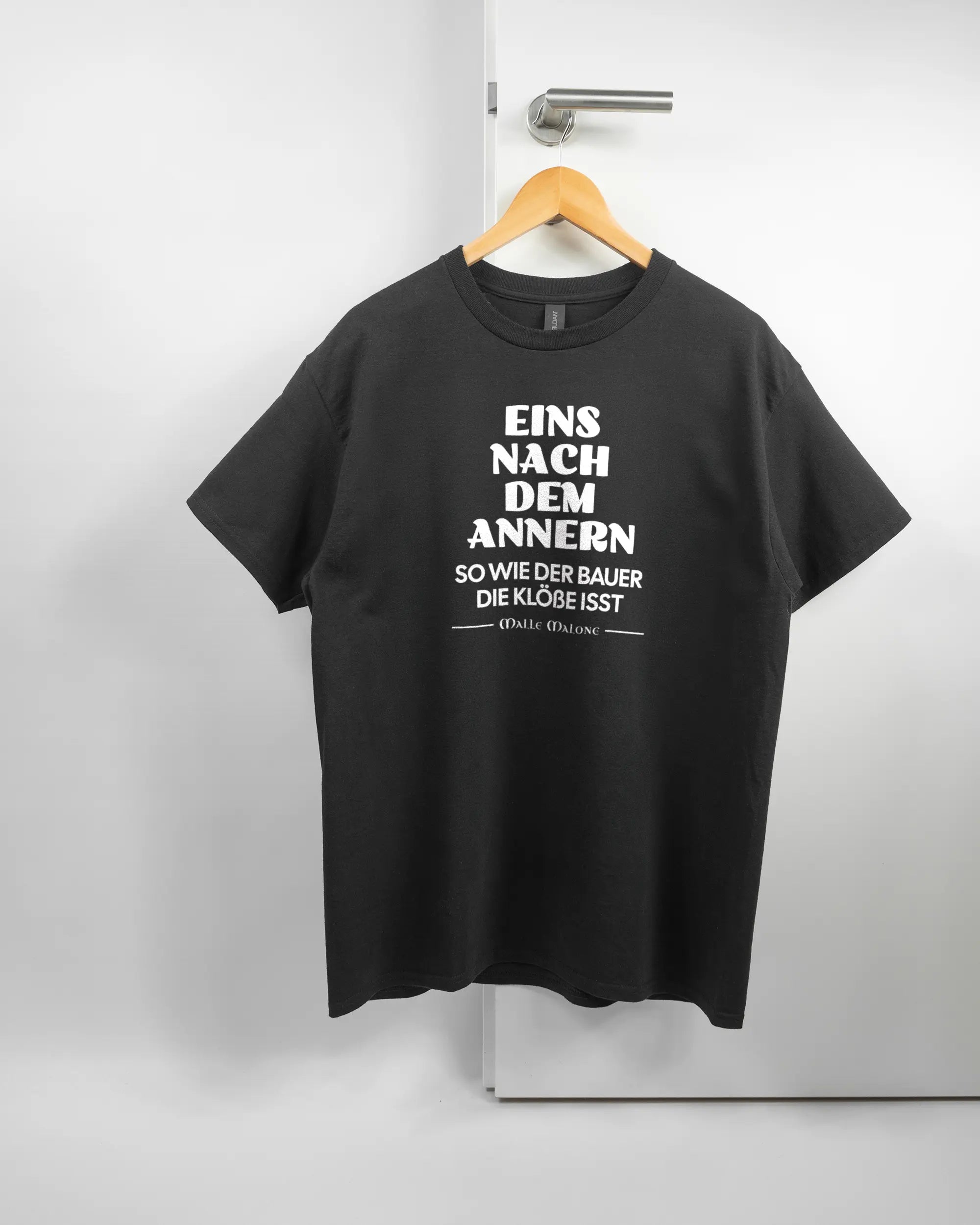 Vorderseite des Basic Unisex T-Shirt Regular von Maondo mit dem Design Eins nach dem Annern in der Farbe Black und in der Größe L auf einem Bügel an der Türklinke aufgehängt