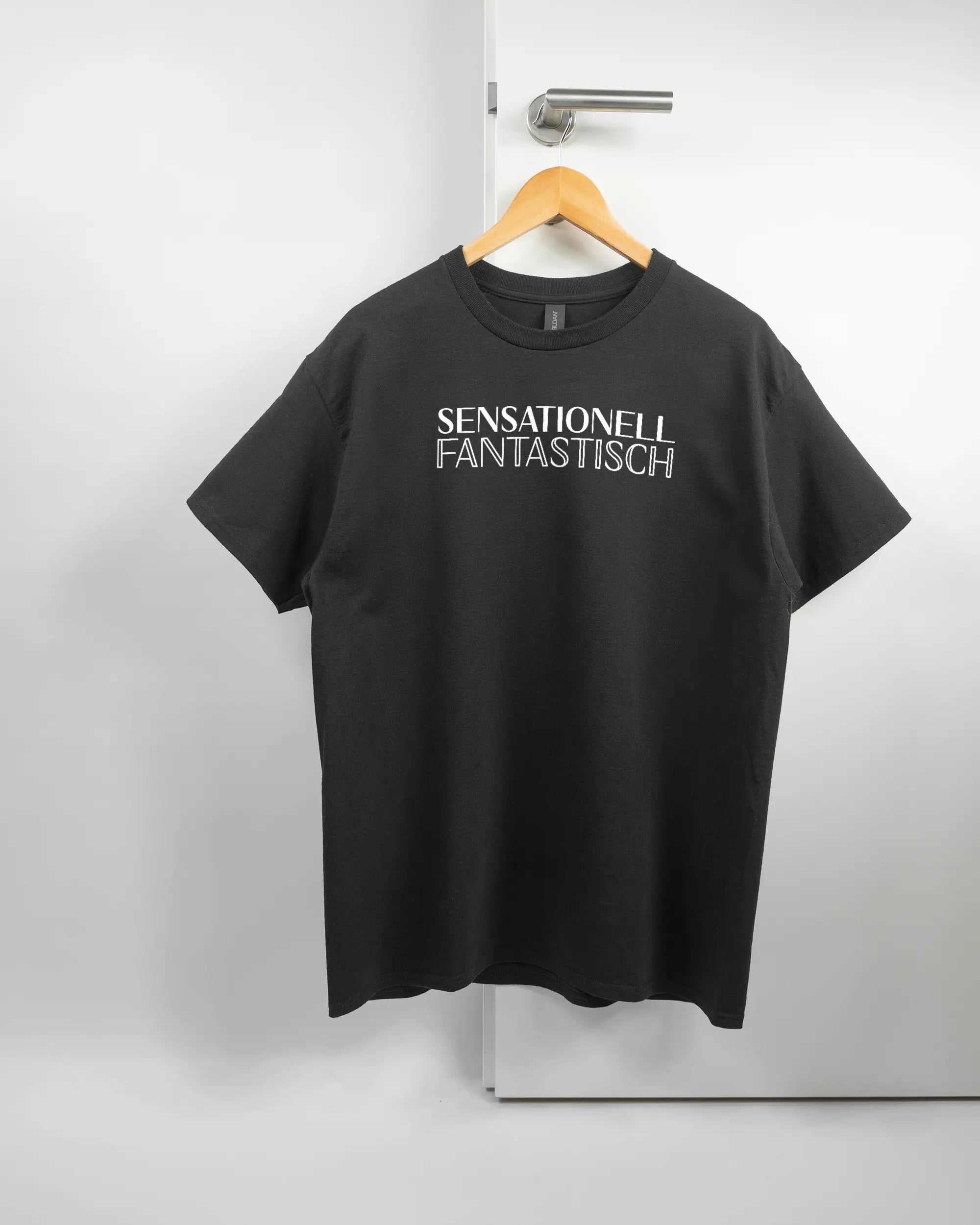 Vorderseite des Basic Unisex T-Shirt Regular von Maondo mit dem Design Sensationell in der Farbe Black und in der Größe L auf einem Bügel an der Türklinke aufgehängt