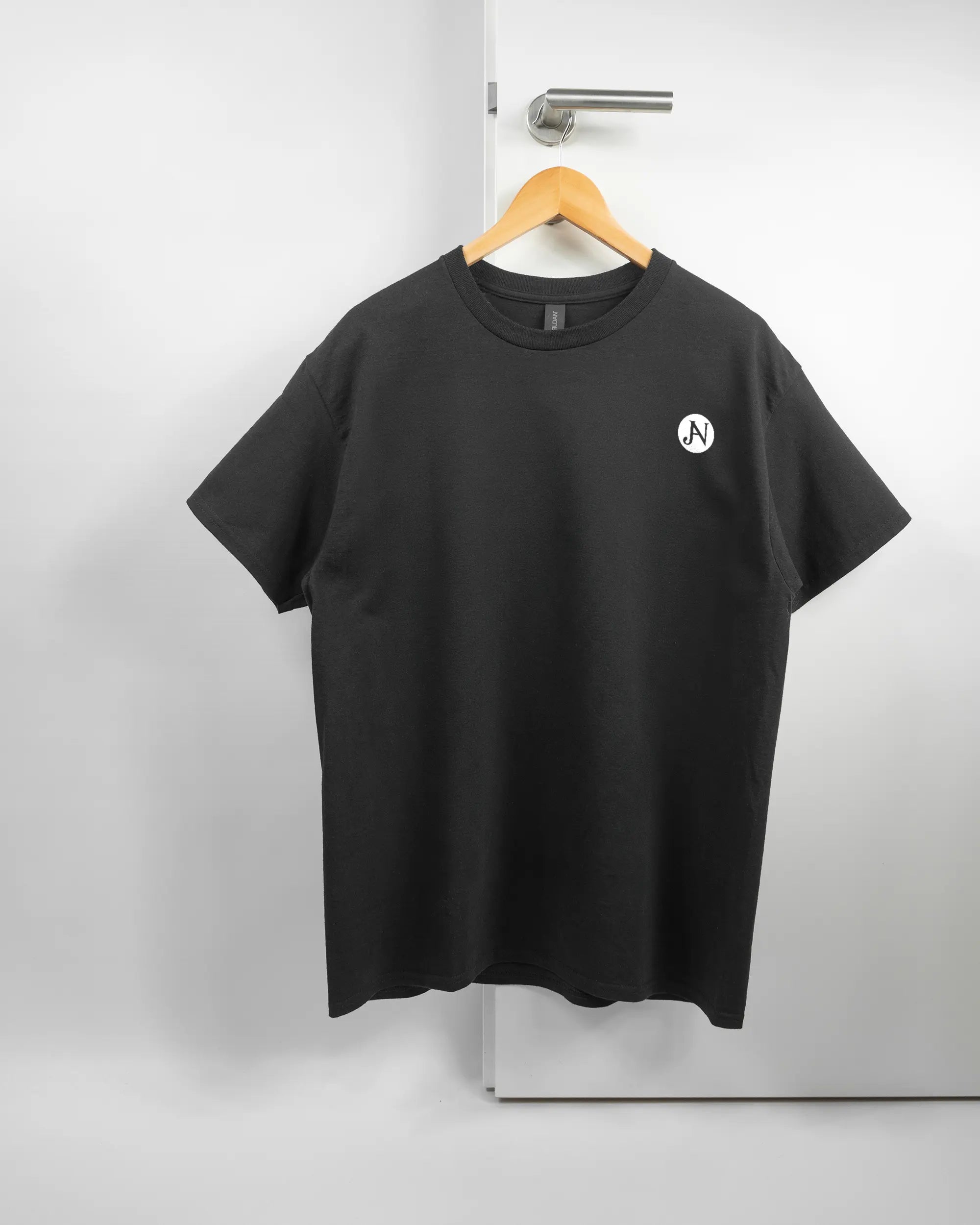 Vorderseite des Basic Unisex T-Shirt Regular von Maondo mit dem Design JB1 in der Farbe Black und in der Größe L auf einem Bügel an der Türklinke aufgehängt