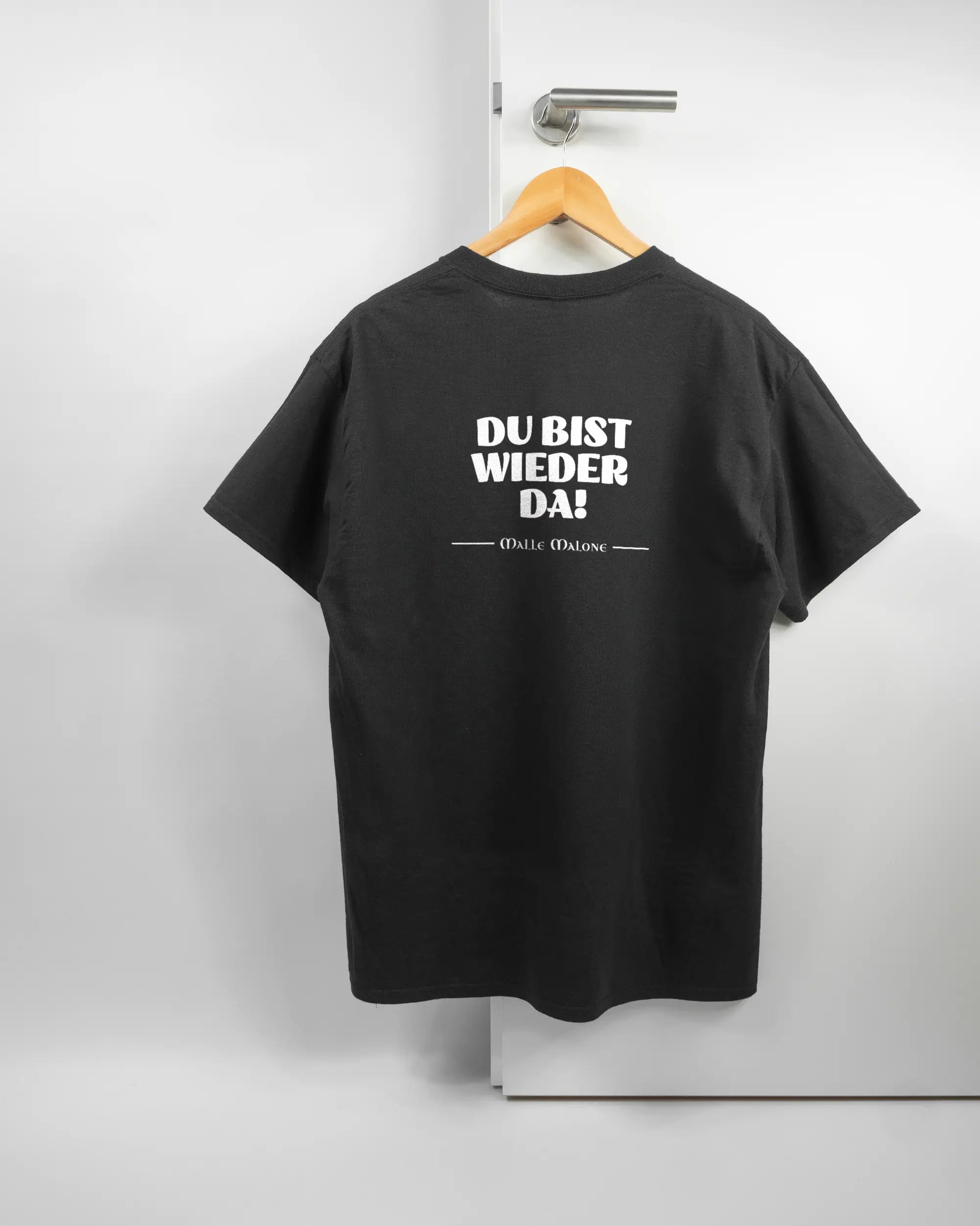 Rückseite des Basic Unisex T-Shirt Regular von Maondo mit dem Design Wieder da in der Farbe Black und in der Größe L auf einem Bügel an der Türklinke aufgehängt