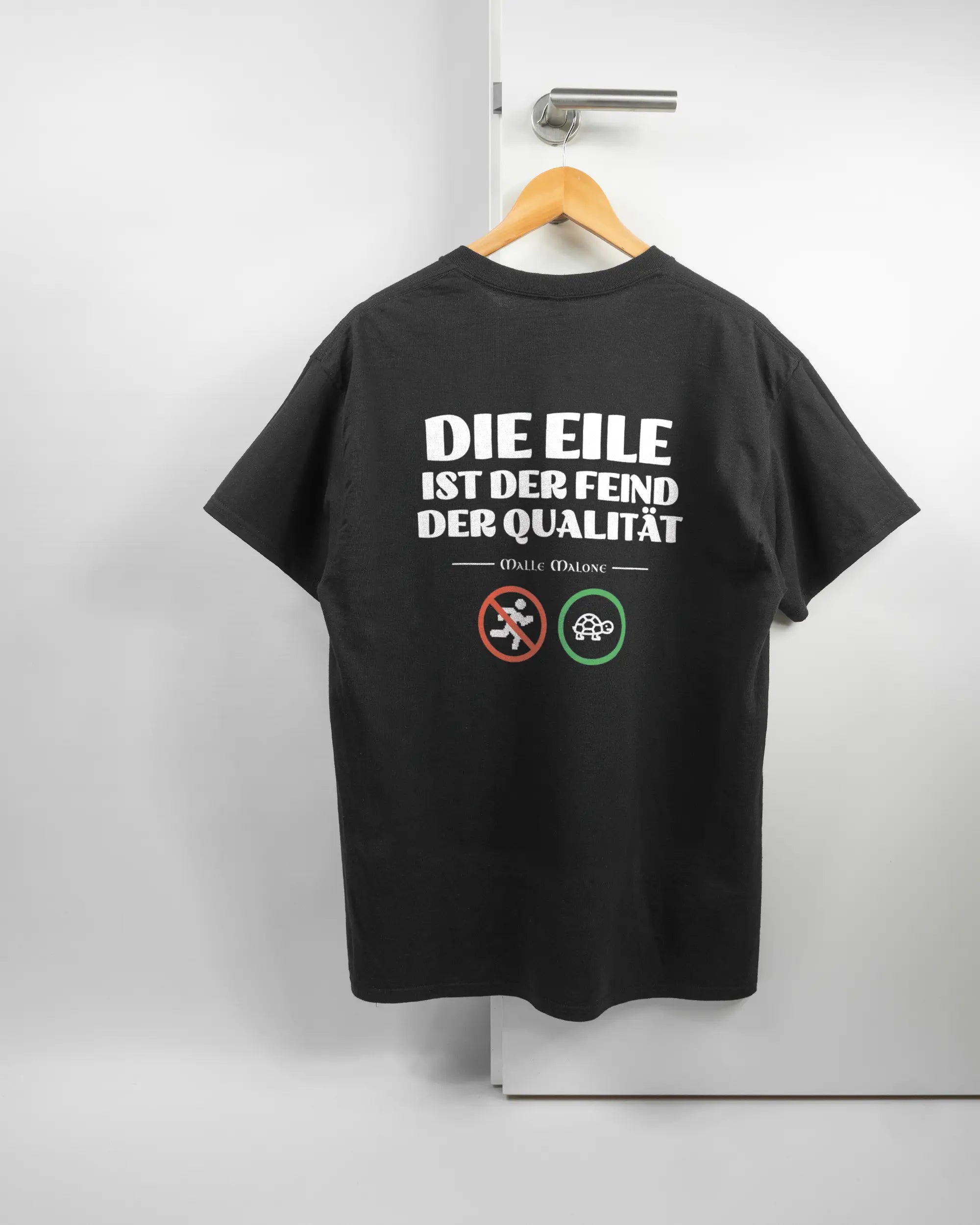 Rückseite des Basic Unisex T-Shirt Regular von Maondo mit dem Design Keine Eile in der Farbe Black und in der Größe L auf einem Bügel an der Türklinke aufgehängt