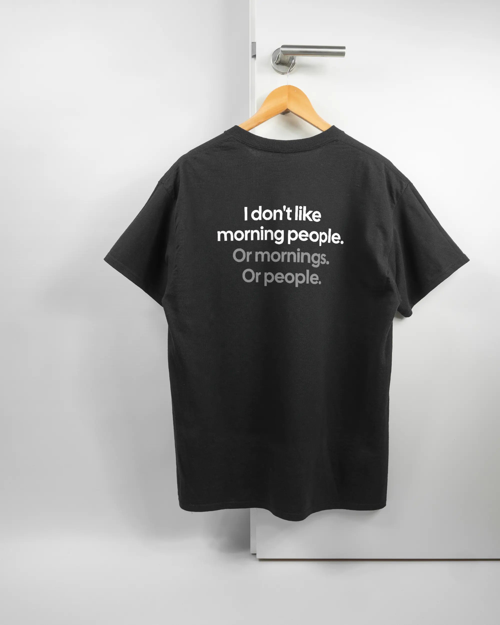 Rückseite des Basic Unisex T-Shirt Regular von Maondo mit dem Design Morning Person in der Farbe Black und in der Größe L auf einem Bügel an der Türklinke aufgehängt