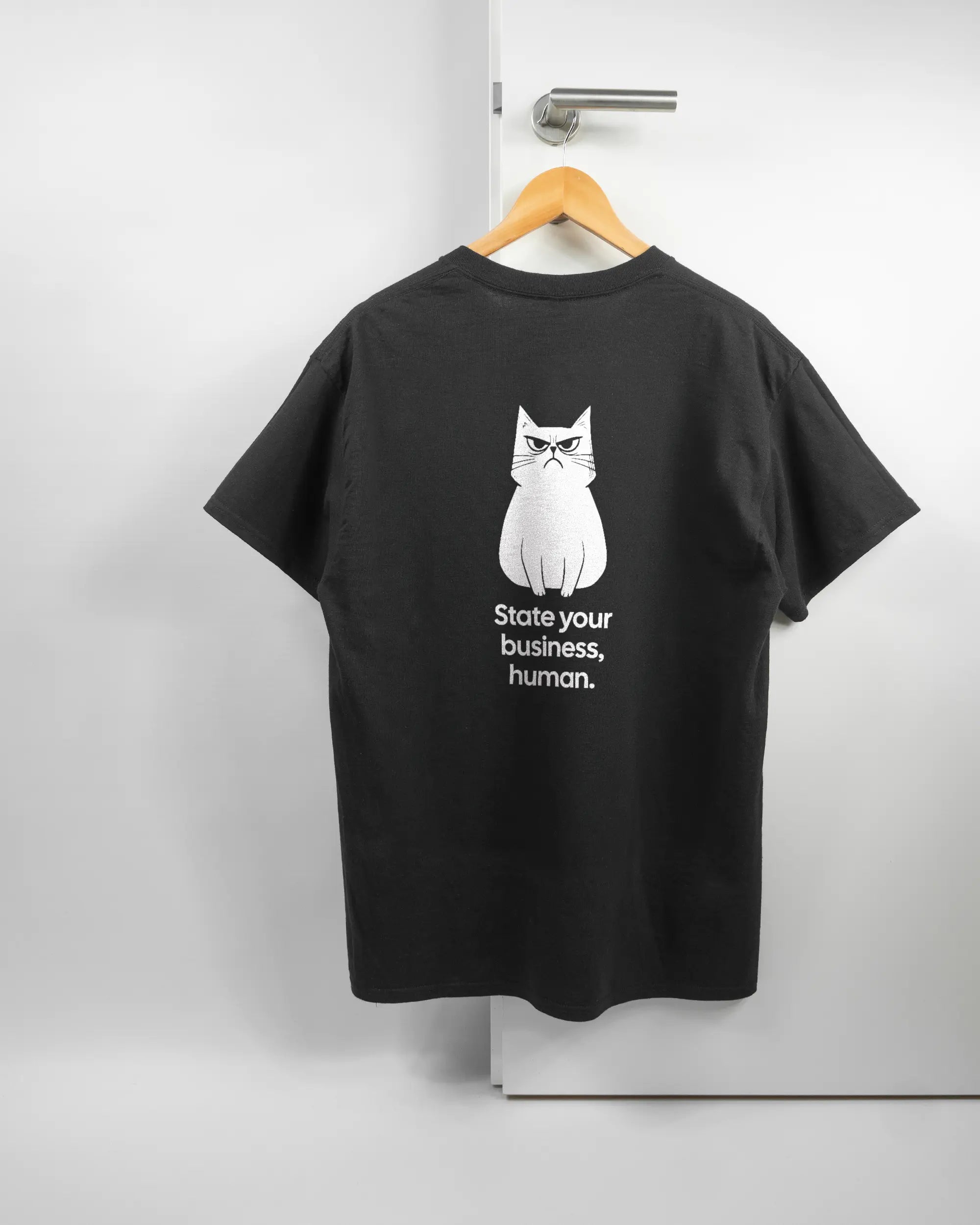 Rückseite des Basic Unisex T-Shirt Regular von Maondo mit dem Design Grumpy Purr in der Farbe Black und in der Größe L auf einem Bügel an der Türklinke aufgehängt