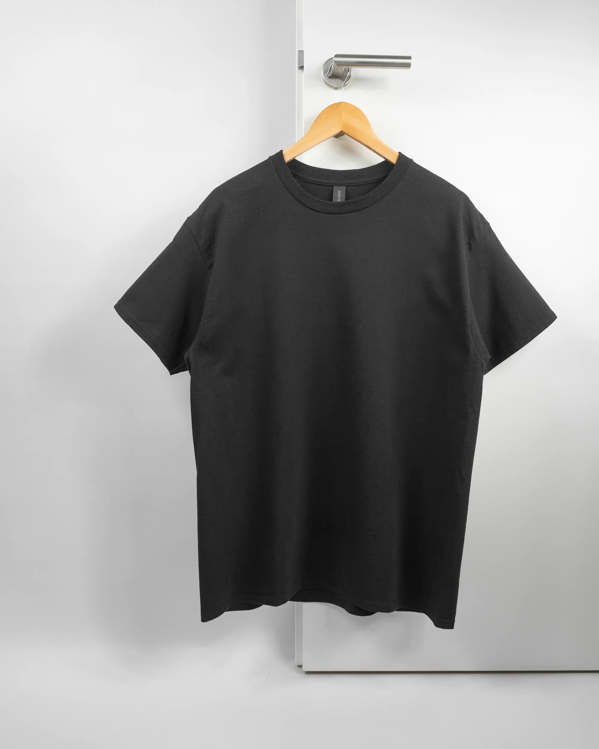 Vorderseite des Basic Unisex T-Shirt Regular von Maondo ohne Motiv in der Farbe Black und in der Größe L auf einem Bügel an der Türklinke aufgehängt