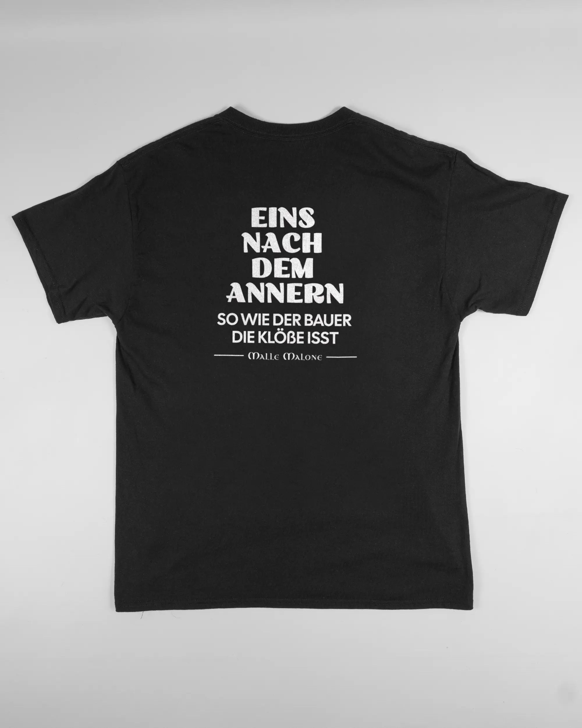 Rückseite des Basic Unisex T-Shirt Regular von Maondo mit dem Design Eins nach dem Annern in der Farbe Black und in der Größe L flach auf den Boden gelegt