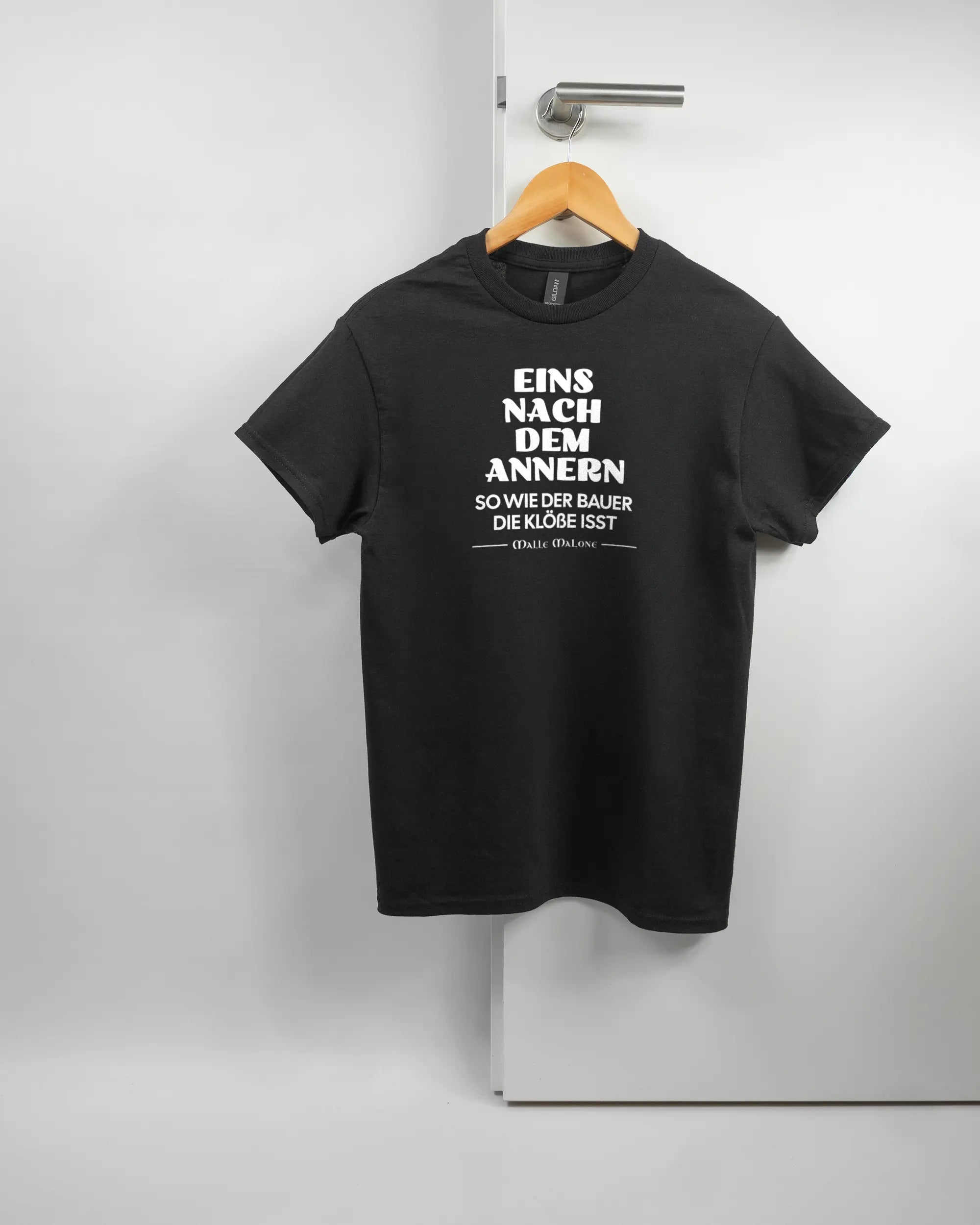 Vorderseite des Basic Unisex T-Shirt Regular von Maondo mit dem Design Eins nach dem Annern in der Farbe Black und in der Größe S auf einem Bügel an der Türklinke aufgehängt
