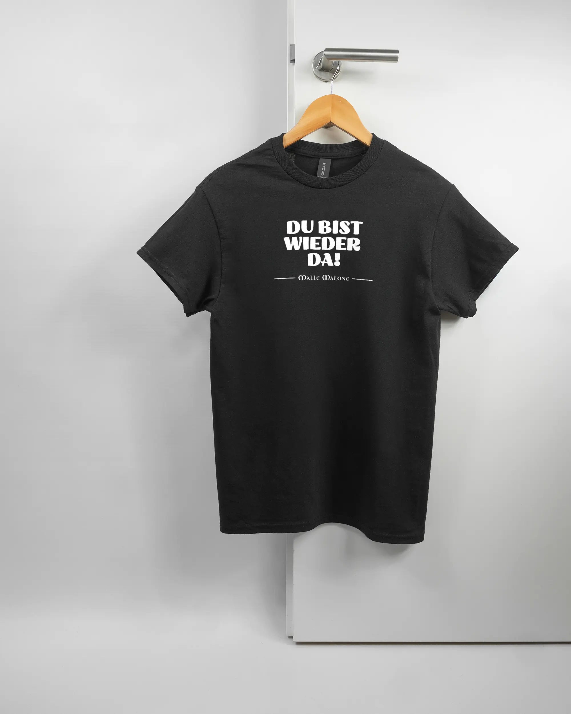 Vorderseite des Basic Unisex T-Shirt Regular von Maondo mit dem Design Wieder da in der Farbe Black und in der Größe S auf einem Bügel an der Türklinke aufgehängt