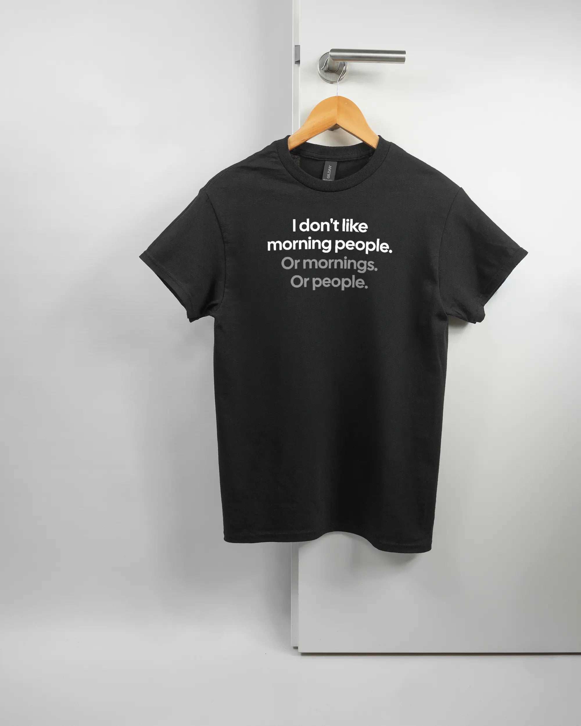 Vorderseite des Basic Unisex T-Shirt Regular von Maondo mit dem Design Morning Person in der Farbe Black und in der Größe S auf einem Bügel an der Türklinke aufgehängt