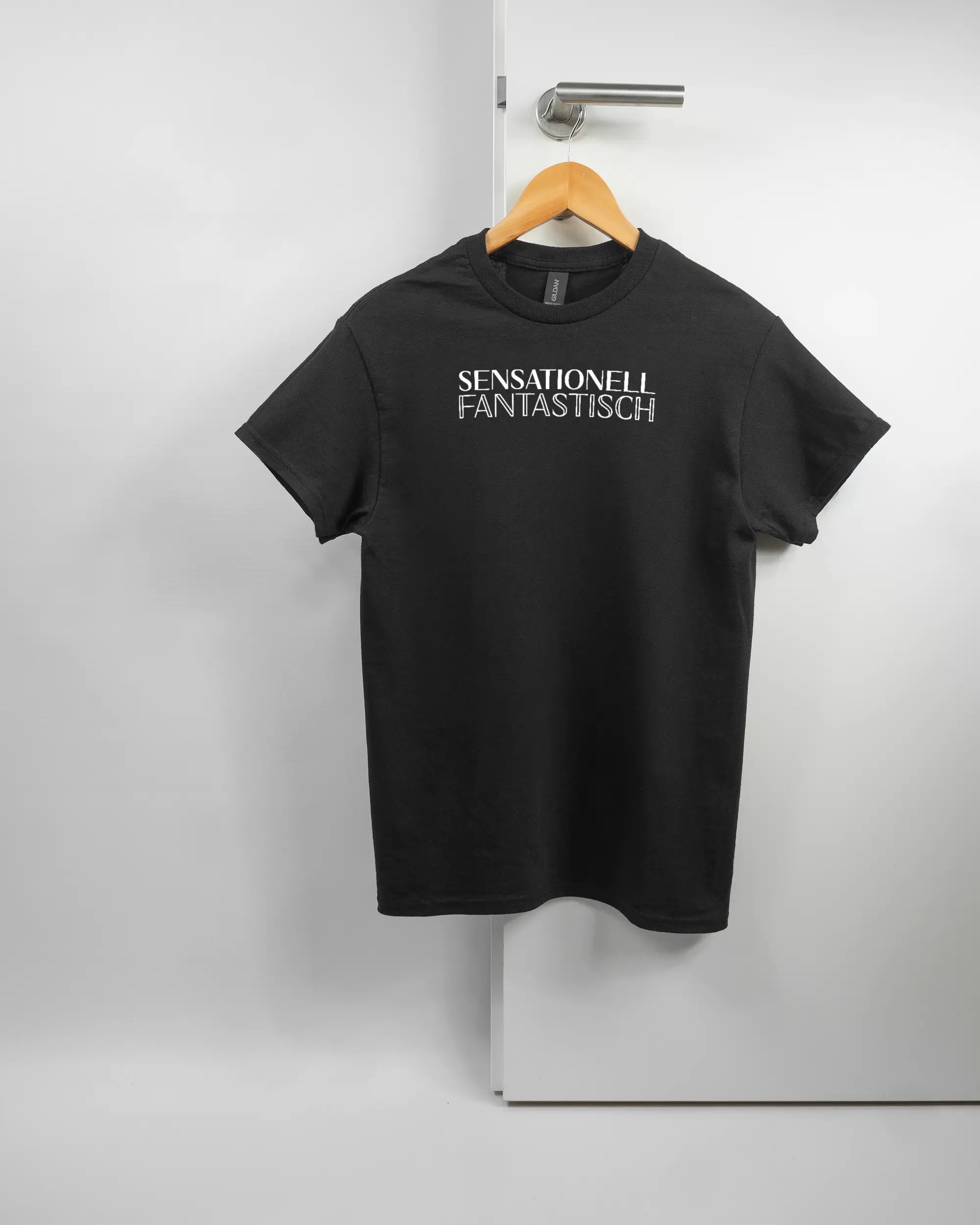 Vorderseite des Basic Unisex T-Shirt Regular von Maondo mit dem Design Sensationell in der Farbe Black und in der Größe S auf einem Bügel an der Türklinke aufgehängt