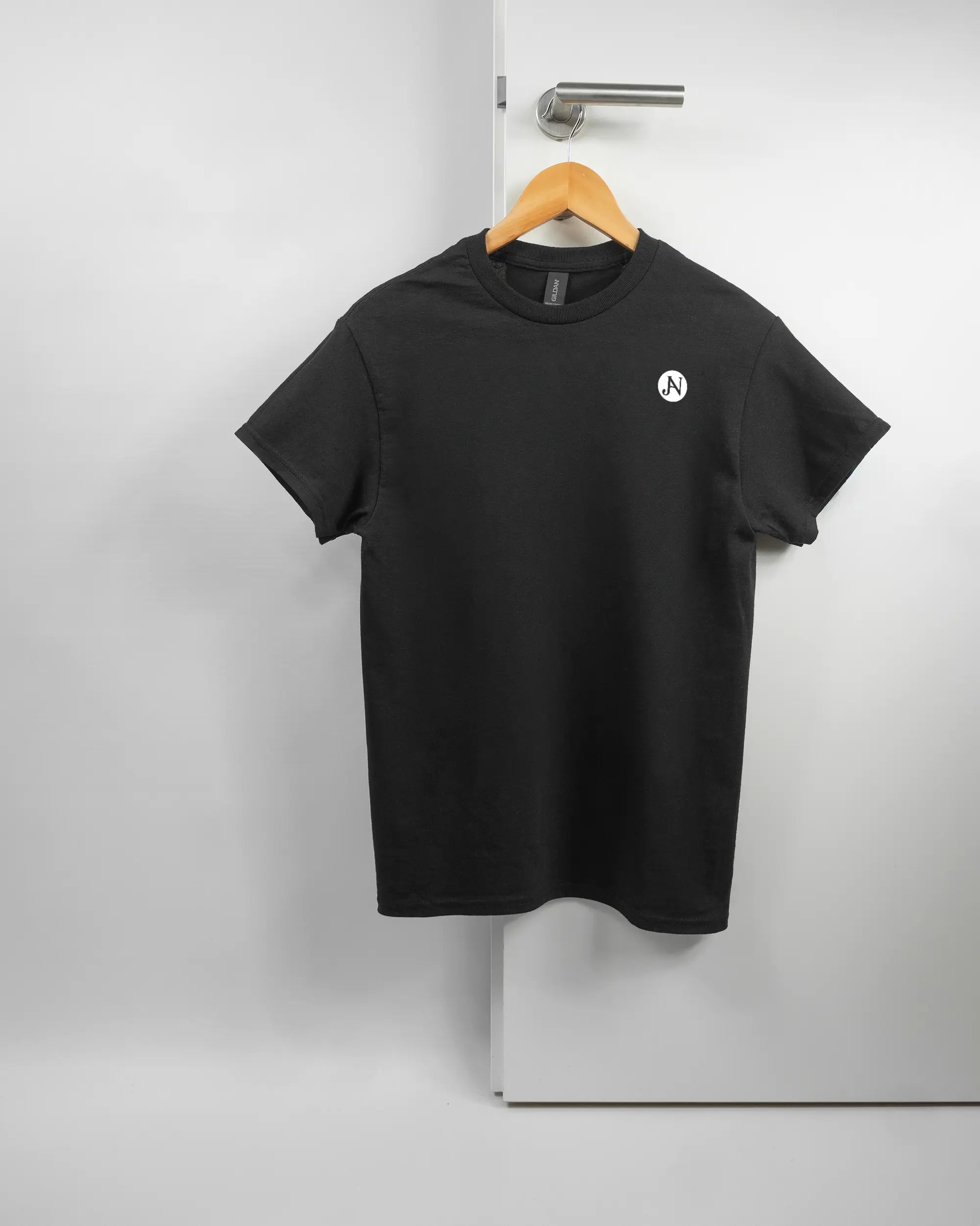 Vorderseite des Basic Unisex T-Shirt Regular von Maondo mit dem Design JB1 in der Farbe Black und in der Größe S auf einem Bügel an der Türklinke aufgehängt