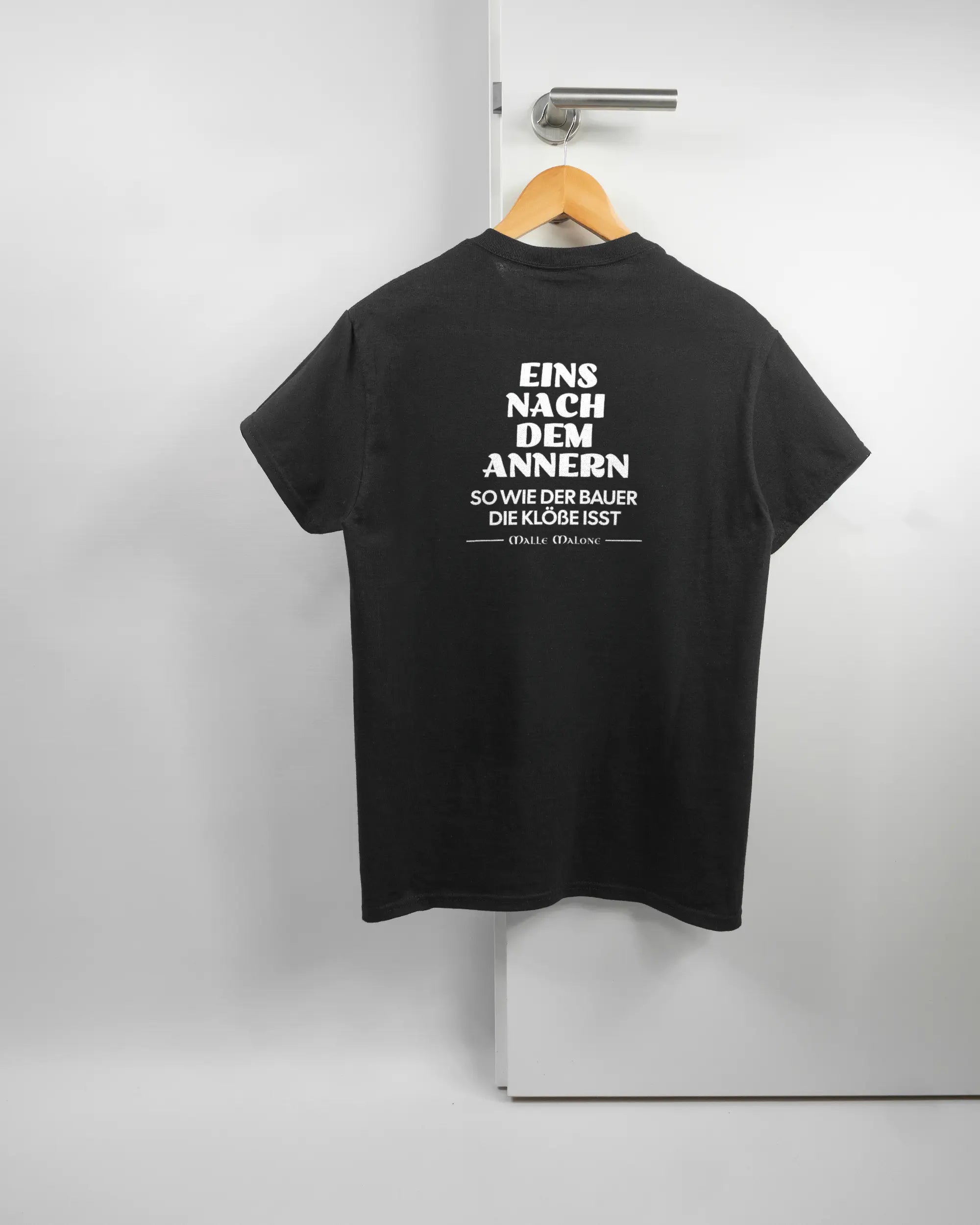 Rückseite des Basic Unisex T-Shirt Regular von Maondo mit dem Design Eins nach dem Annern in der Farbe Black und in der Größe S auf einem Bügel an der Türklinke aufgehängt