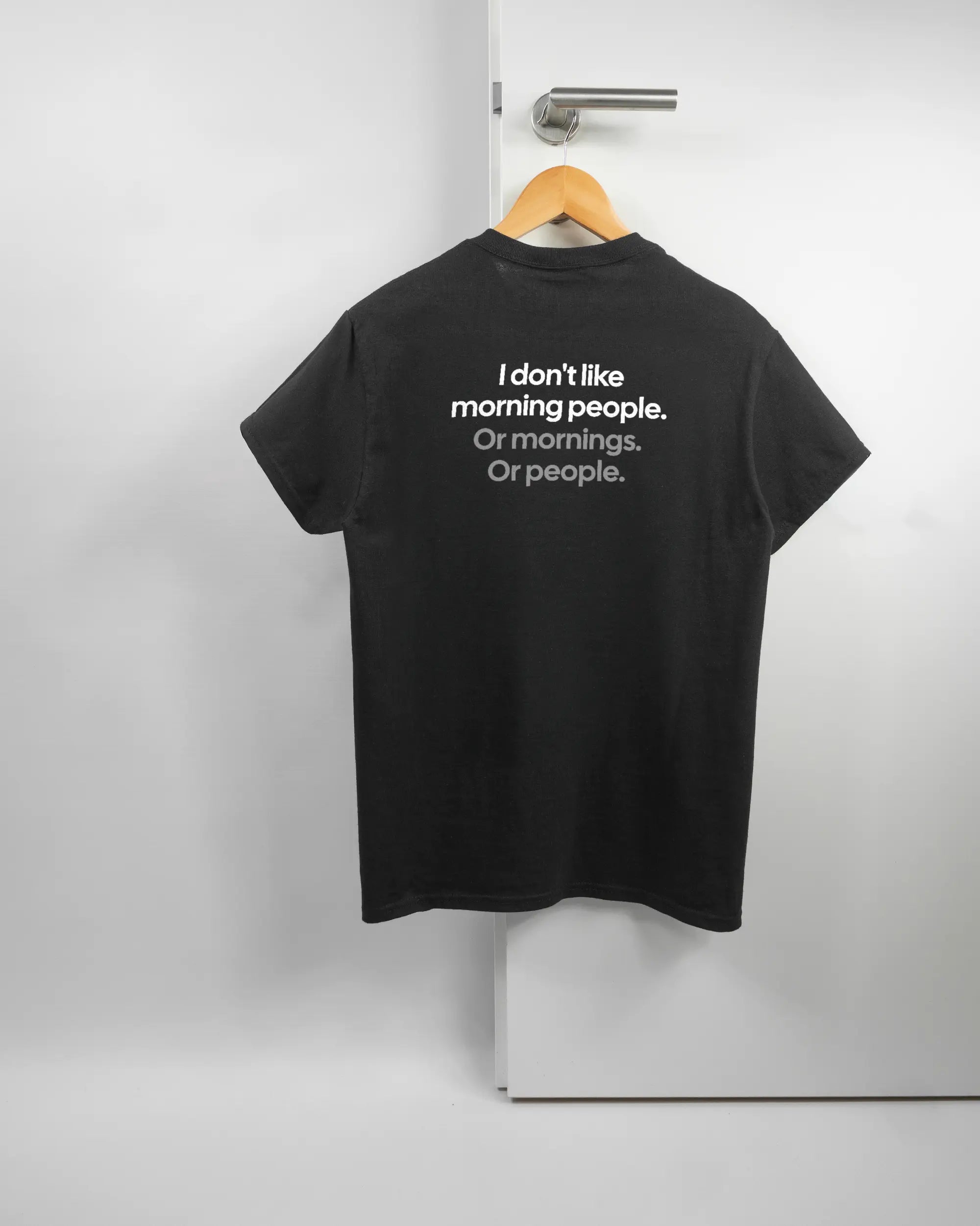 Rückseite des Basic Unisex T-Shirt Regular von Maondo mit dem Design Morning Person in der Farbe Black und in der Größe S auf einem Bügel an der Türklinke aufgehängt