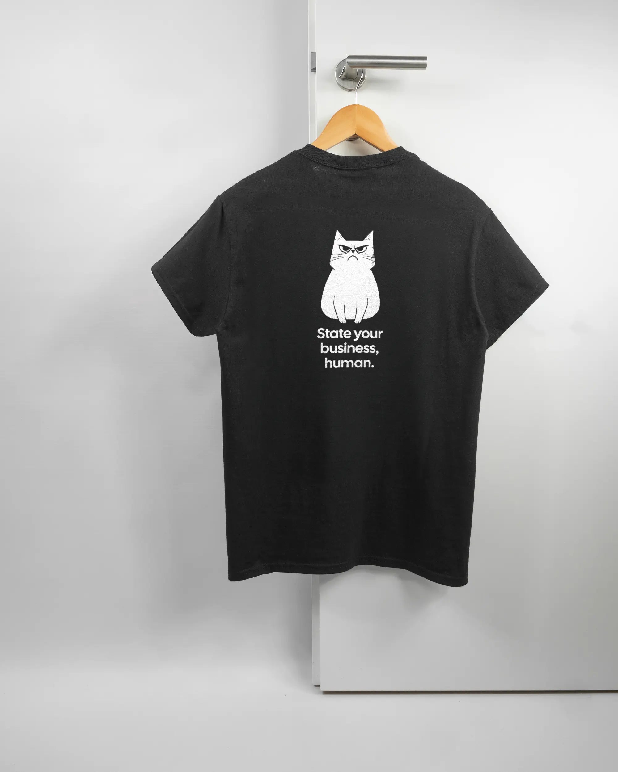 Rückseite des Basic Unisex T-Shirt Regular von Maondo mit dem Design Grumpy Purr in der Farbe Black und in der Größe S auf einem Bügel an der Türklinke aufgehängt