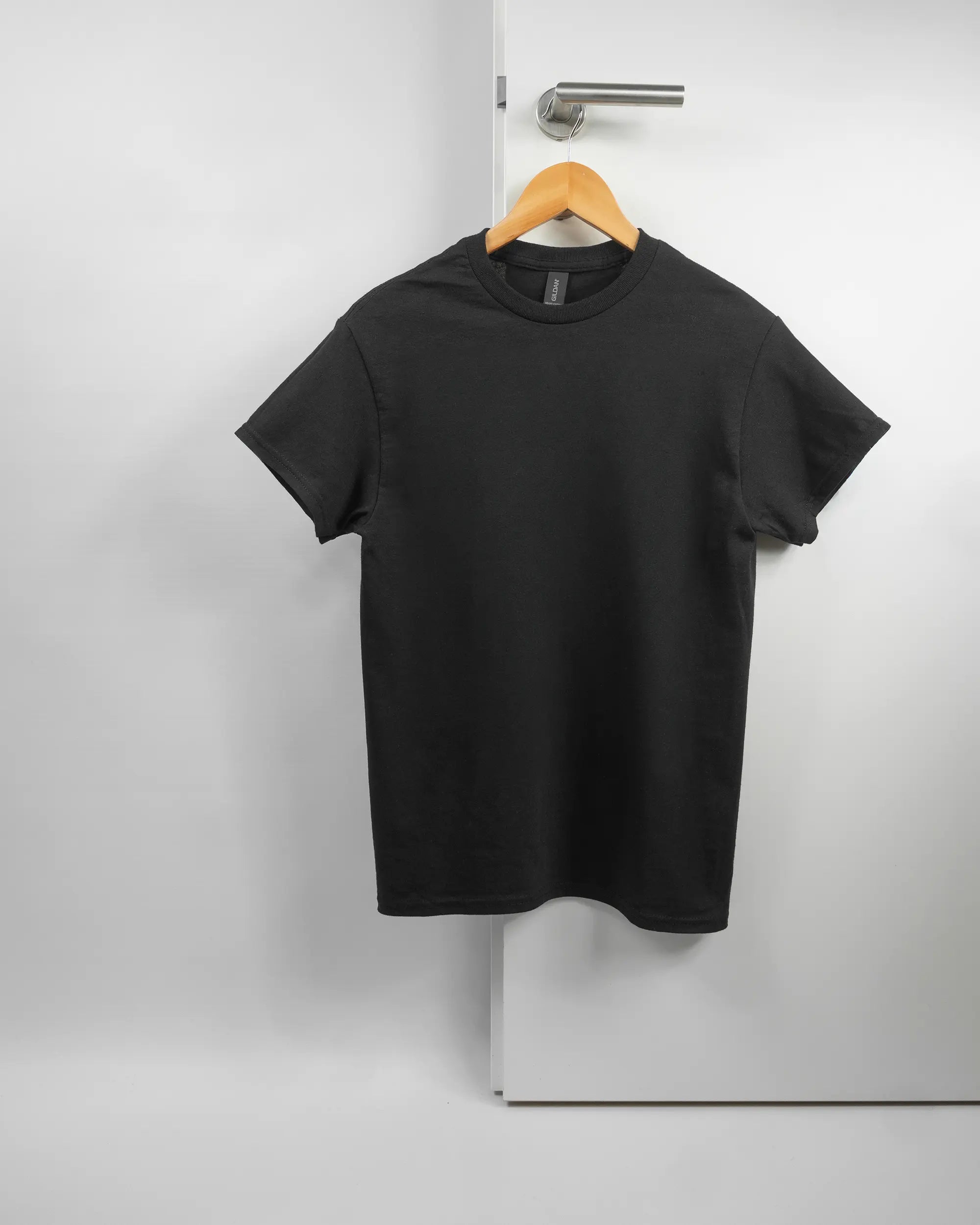 Vorderseite des Basic Unisex T-Shirt Regular von Maondo ohne Motiv in der Farbe Black und in der Größe S auf einem Bügel an der Türklinke aufgehängt
