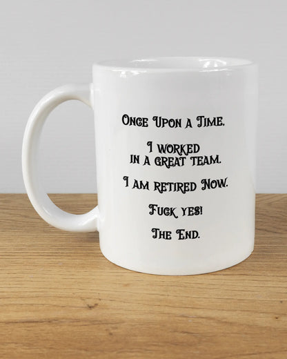 Titelbild, das die linke Seite der beidseitig bedruckten Keramiktasse von Maondo mit dem Design Finally Retired in der Farbe White auf einem Holztisch zeigt