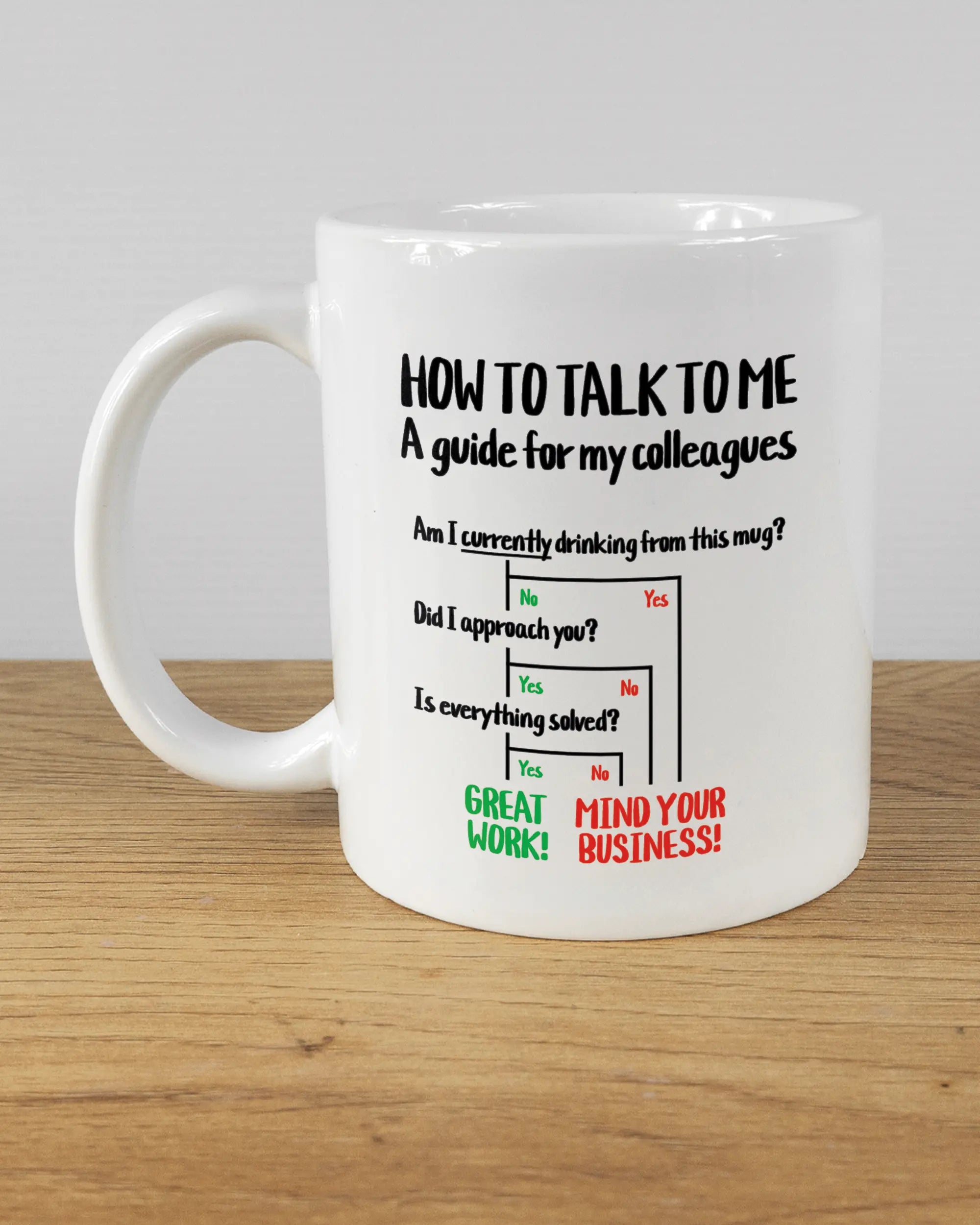 Titelbild, das die linke Seite der beidseitig bedruckten Keramiktasse von Maondo mit dem Design Colleagues Guide in der Farbe White auf einem Holztisch zeigt