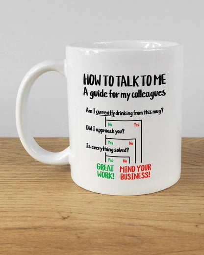 Titelbild, das die linke Seite der beidseitig bedruckten Keramiktasse von Maondo mit dem Design Colleagues Guide in der Farbe White auf einem Holztisch zeigt