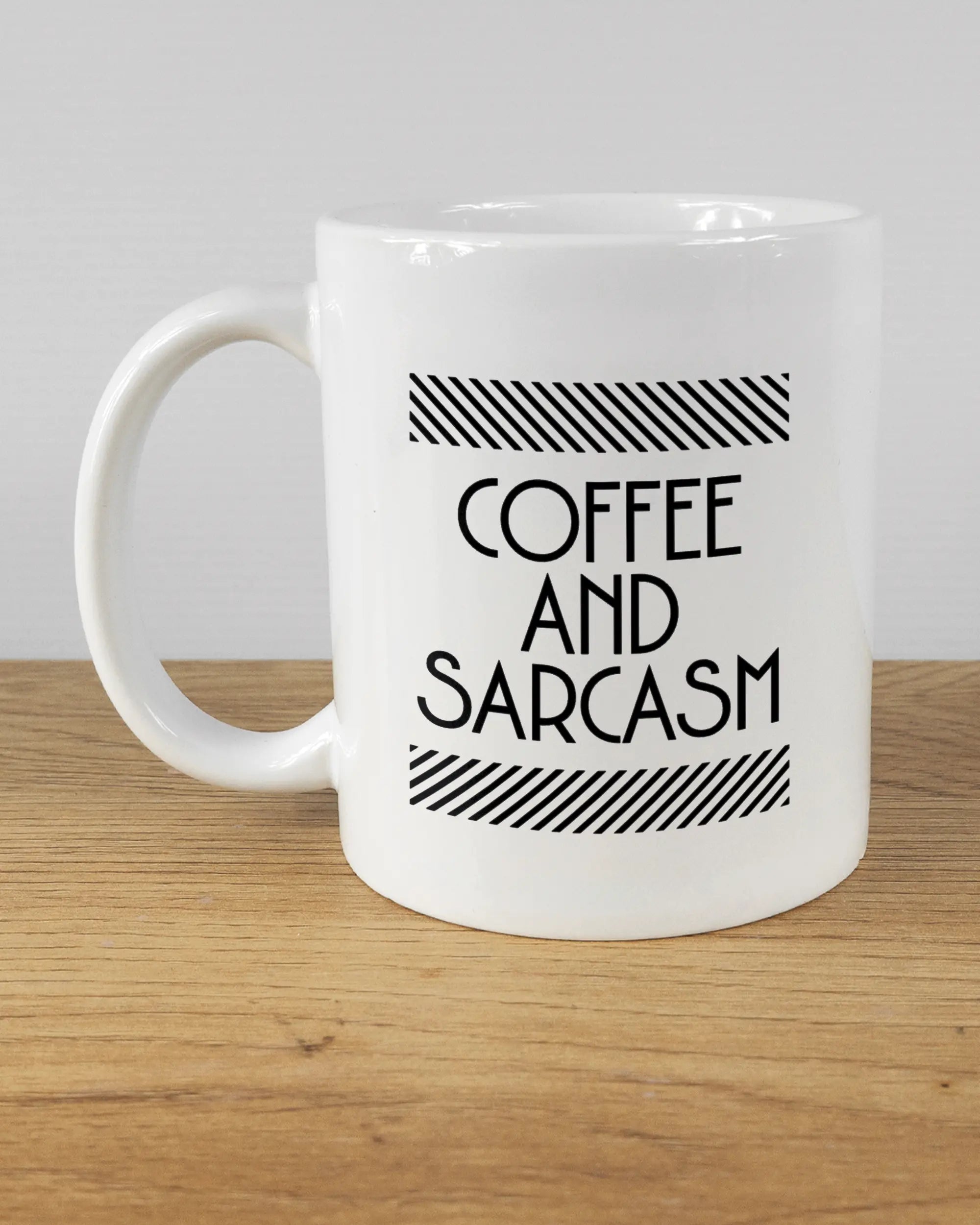 Titelbild, das die linke Seite der beidseitig bedruckten Keramiktasse von Maondo mit dem Design Sarcastic Cup in der Farbe White auf einem Holztisch zeigt