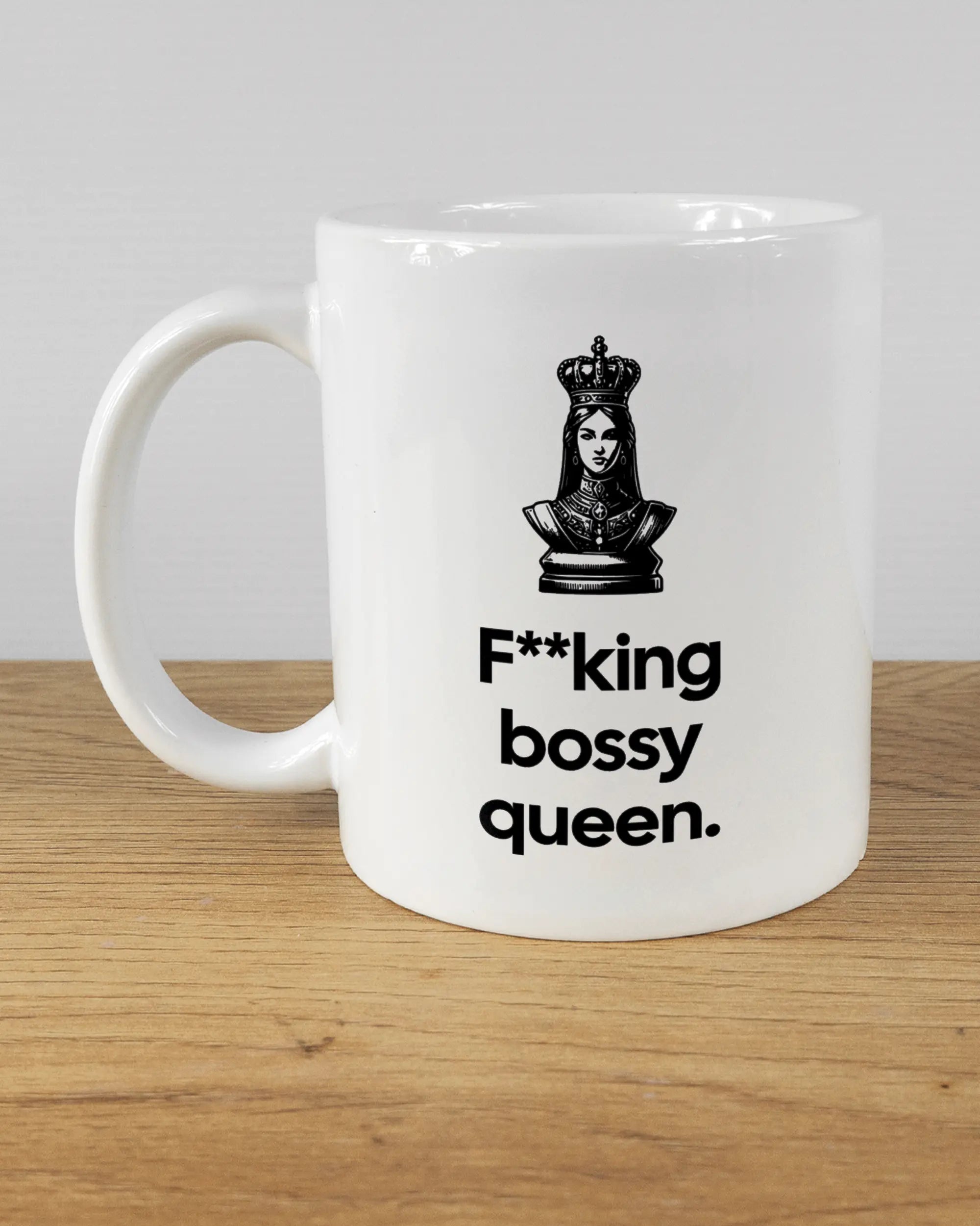 Titelbild, das die linke Seite der beidseitig bedruckten Keramiktasse von Maondo mit dem Design Bossy Queen in der Farbe White auf einem Holztisch zeigt