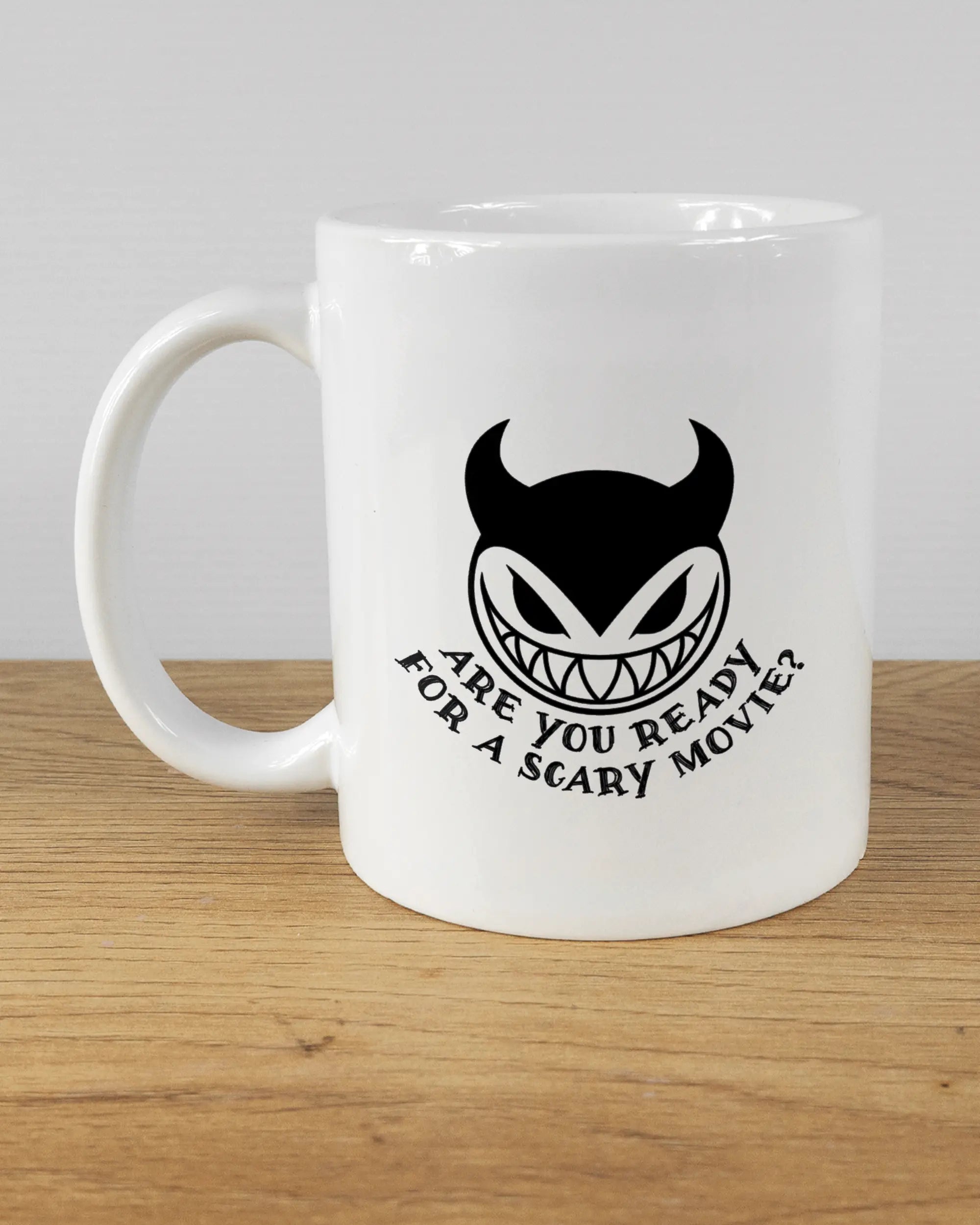 Titelbild, das die linke Seite der beidseitig bedruckten Keramiktasse von Maondo mit dem Design Scary Movie in der Farbe White auf einem Holztisch zeigt