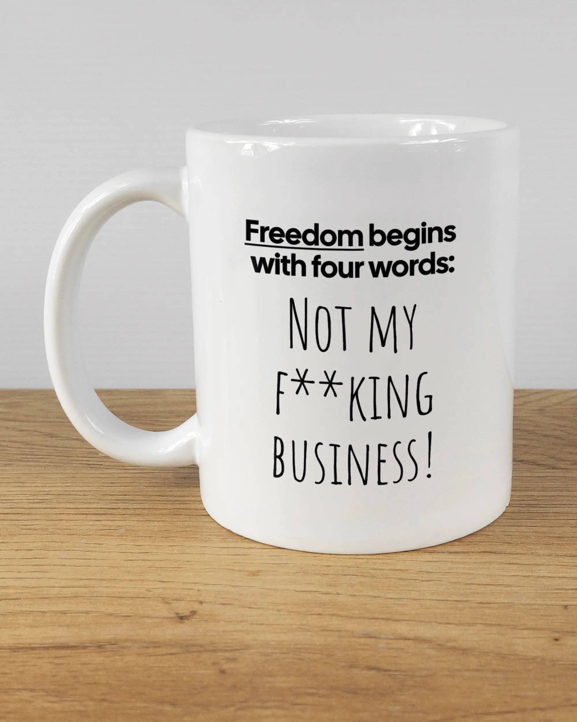 Titelbild, das die linke Seite der beidseitig bedruckten Keramiktasse von Maondo mit dem Design 4 Freedom in der Farbe White auf einem Holztisch zeigt