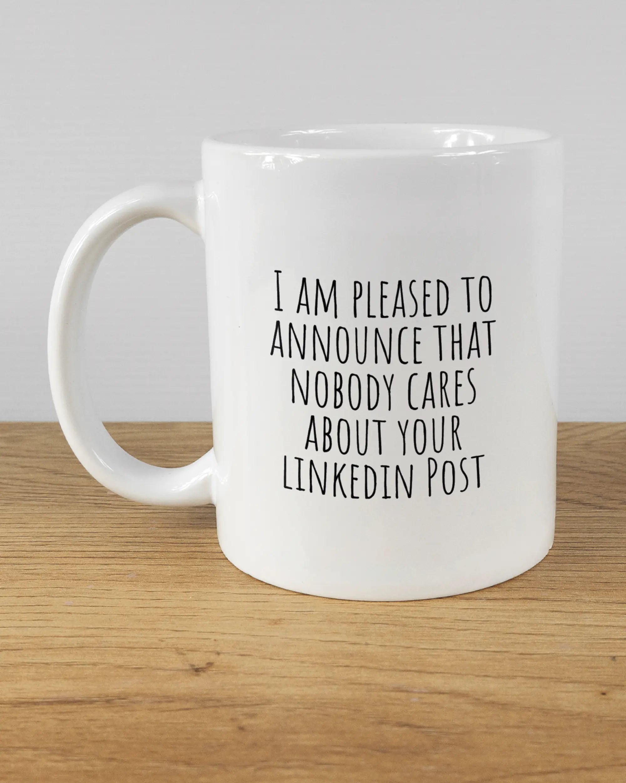 Titelbild, das die linke Seite der beidseitig bedruckten Keramiktasse von Maondo mit dem Design Please Unannounce in der Farbe White auf einem Holztisch zeigt