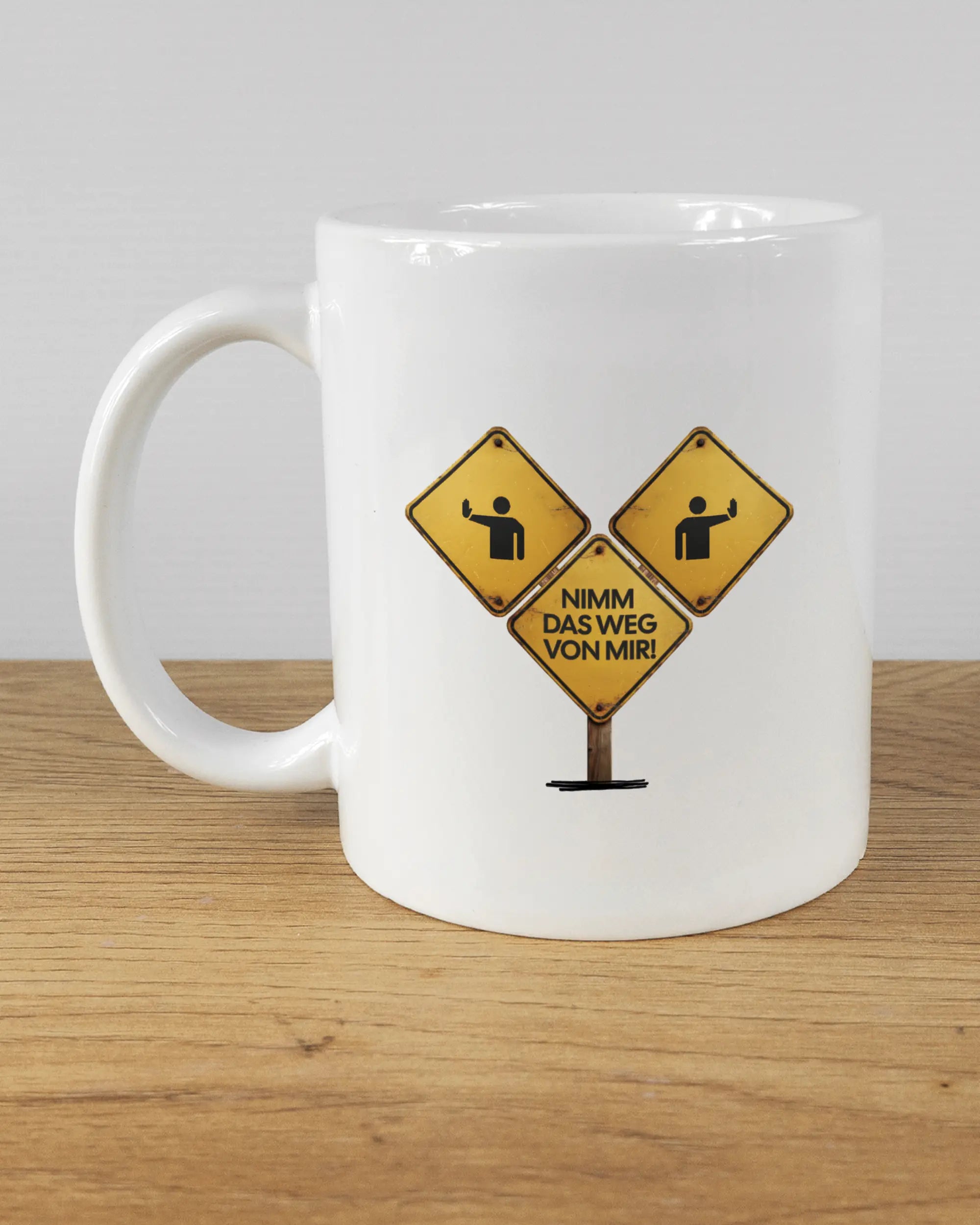 Titelbild, das die linke Seite der beidseitig bedruckten Keramiktasse von Maondo mit dem Design Schutzschild in der Farbe White auf einem Holztisch zeigt