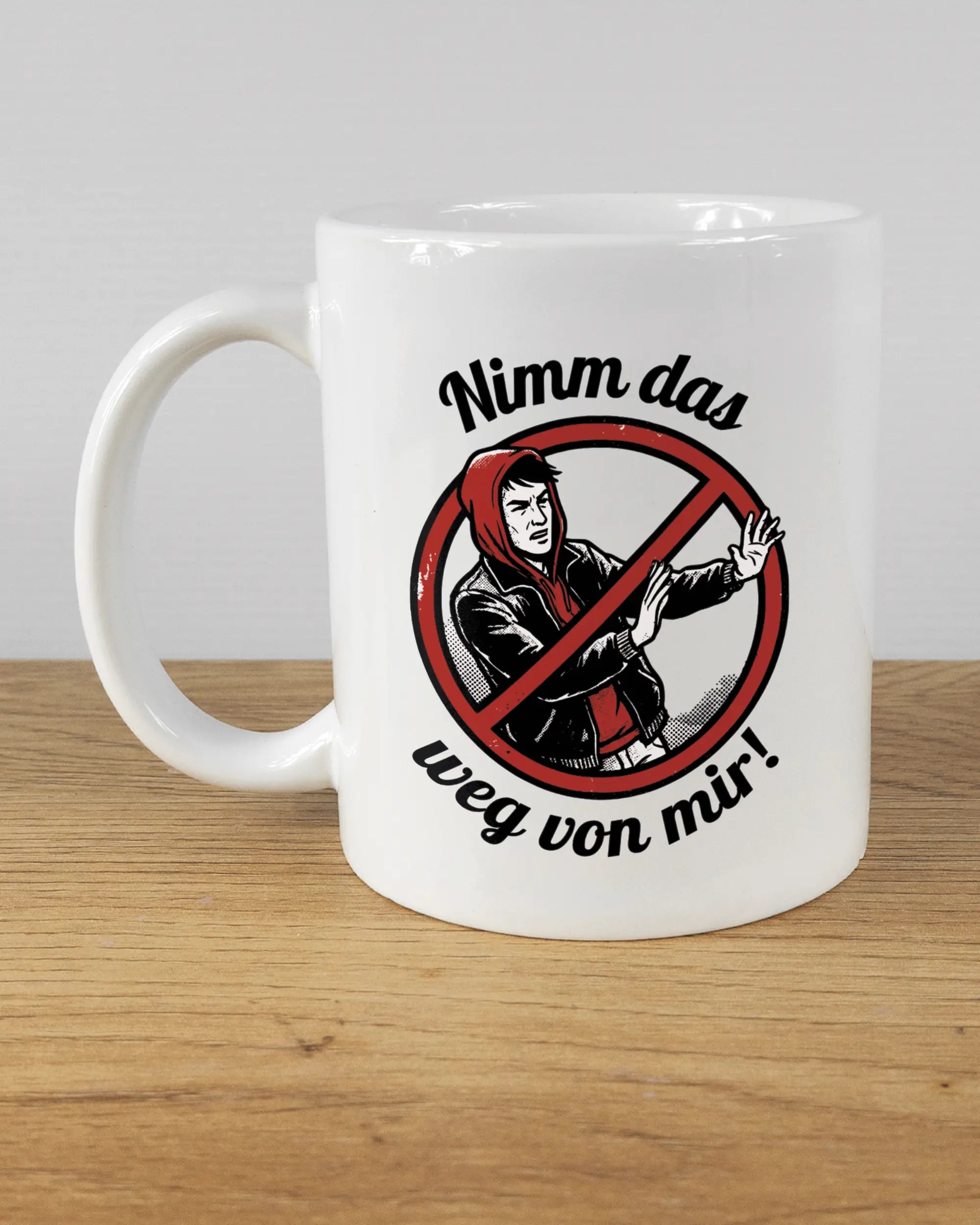 Titelbild, das die linke Seite der beidseitig bedruckten Keramiktasse von Maondo mit dem Design Nimm das weg in der Farbe White auf einem Holztisch zeigt