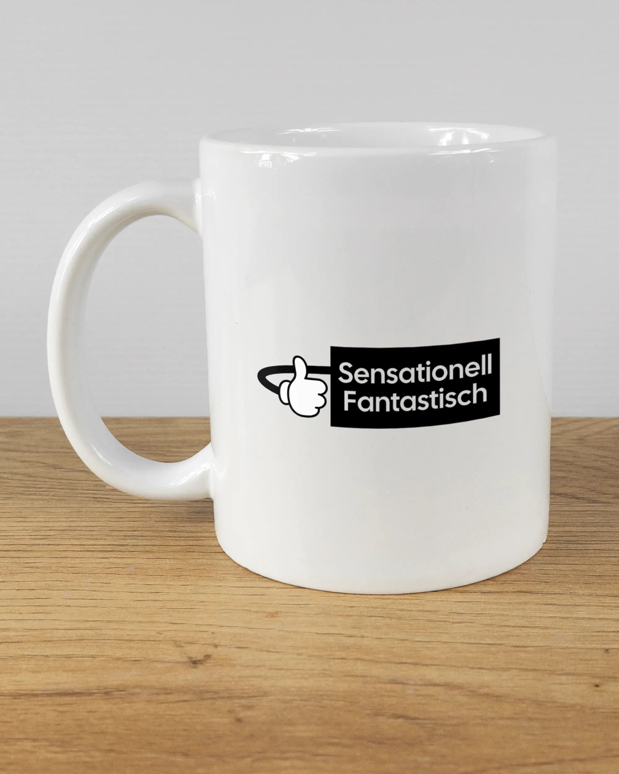 Titelbild, das die linke Seite der beidseitig bedruckten Keramiktasse von Maondo mit dem Design Fantastisch in der Farbe White auf einem Holztisch zeigt