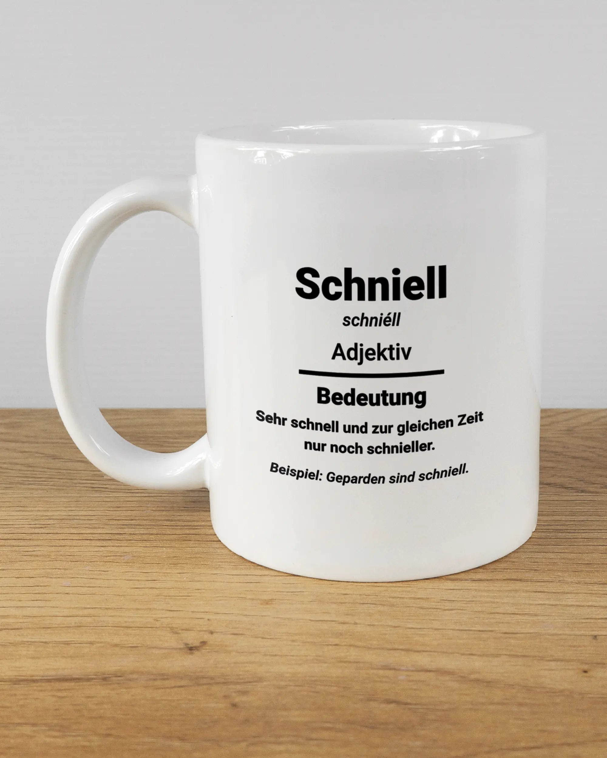 Titelbild, das die linke Seite der beidseitig bedruckten Keramiktasse von Maondo mit dem Design Schniell in der Farbe White auf einem Holztisch zeigt