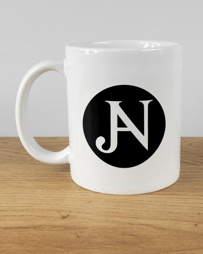 Titelbild, das die linke Seite der beidseitig bedruckten Keramiktasse von Maondo mit dem Design JB1 in der Farbe White auf einem Holztisch zeigt