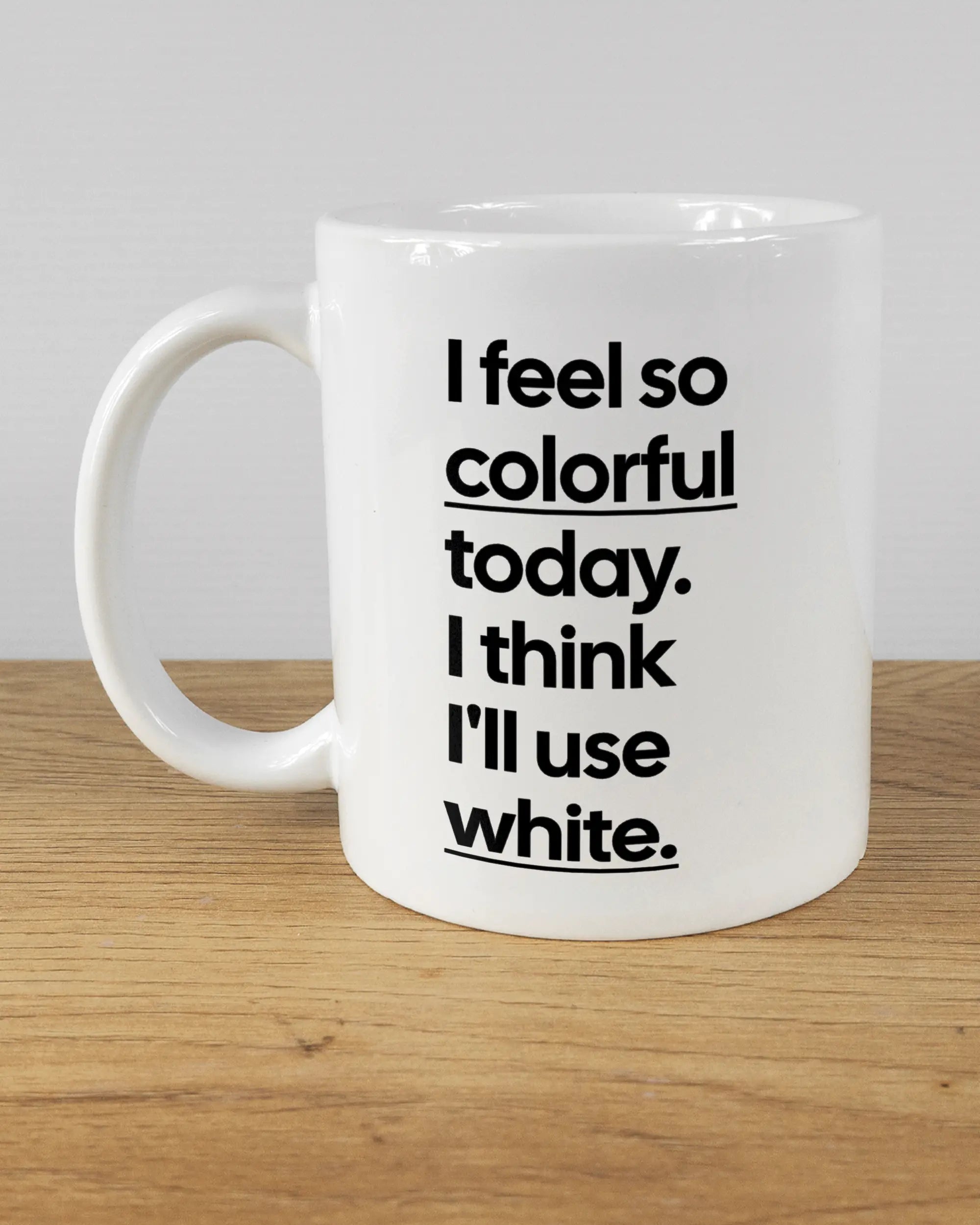 Titelbild, das die linke Seite der beidseitig bedruckten Keramiktasse von Maondo mit dem Design Colorful Day in der Farbe White auf einem Holztisch zeigt