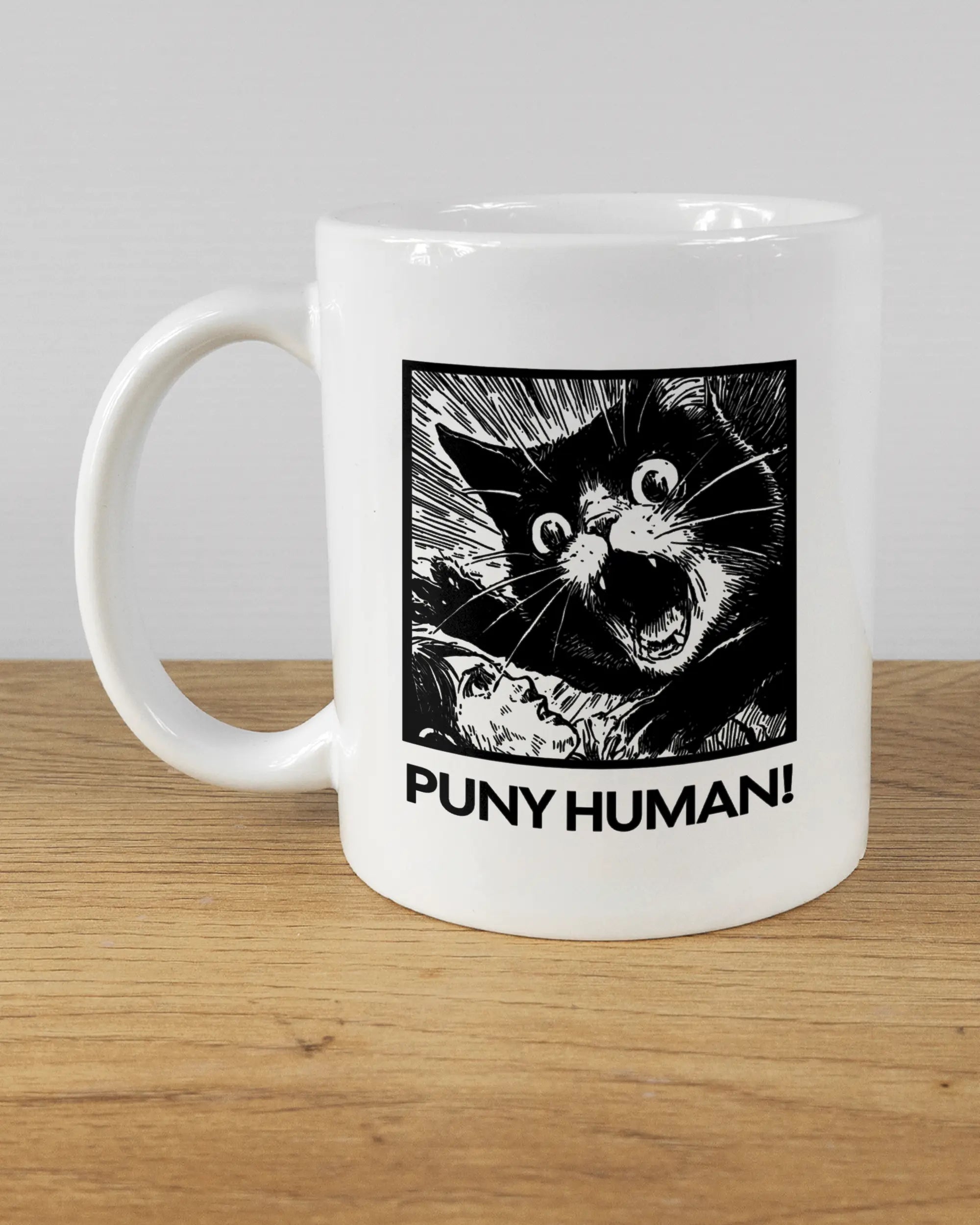 Titelbild, das die linke Seite der beidseitig bedruckten Keramiktasse von Maondo mit dem Design Puny Human in der Farbe White auf einem Holztisch zeigt