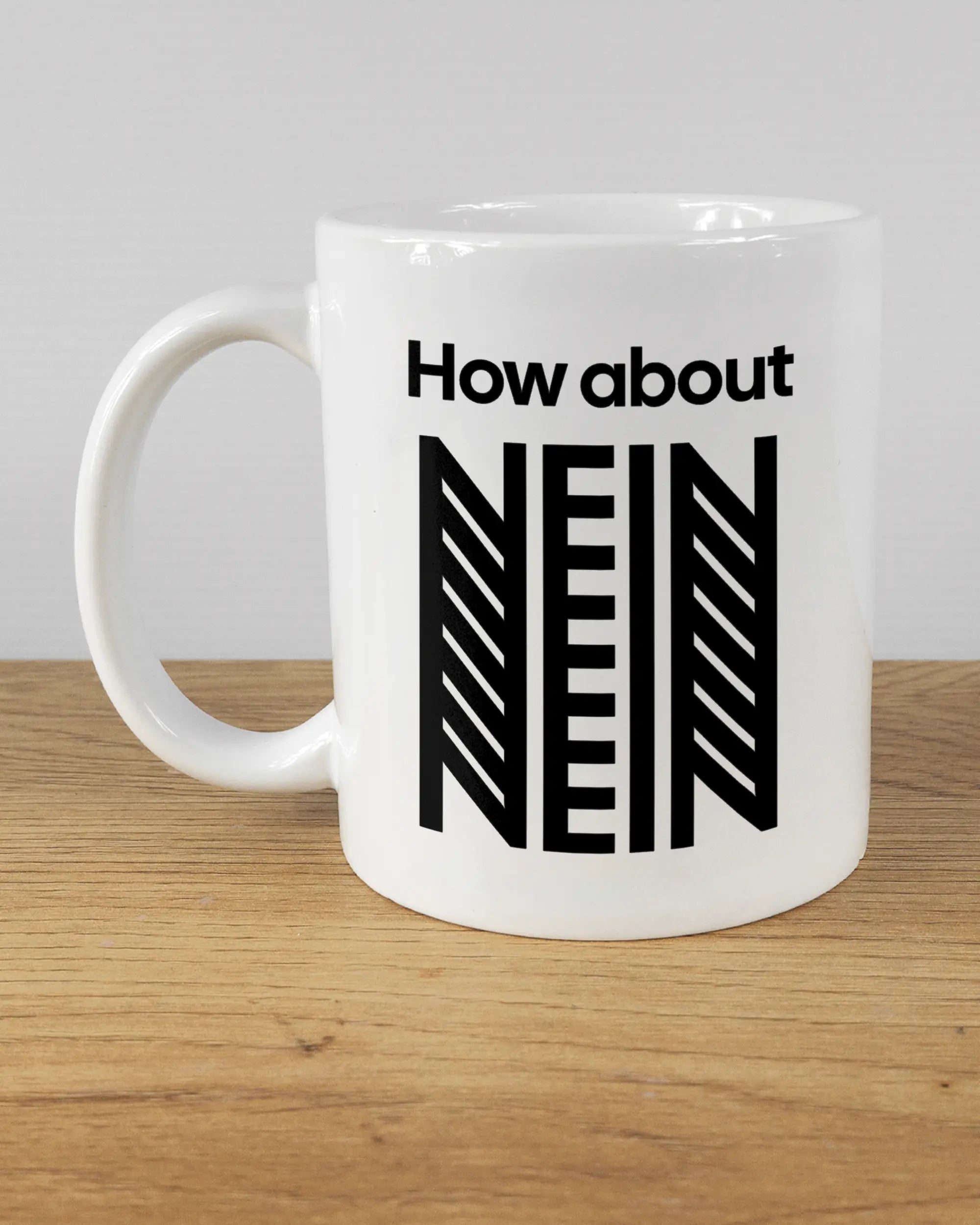 Titelbild, das die linke Seite der beidseitig bedruckten Keramiktasse von Maondo mit dem Design How about nein in der Farbe White auf einem Holztisch zeigt