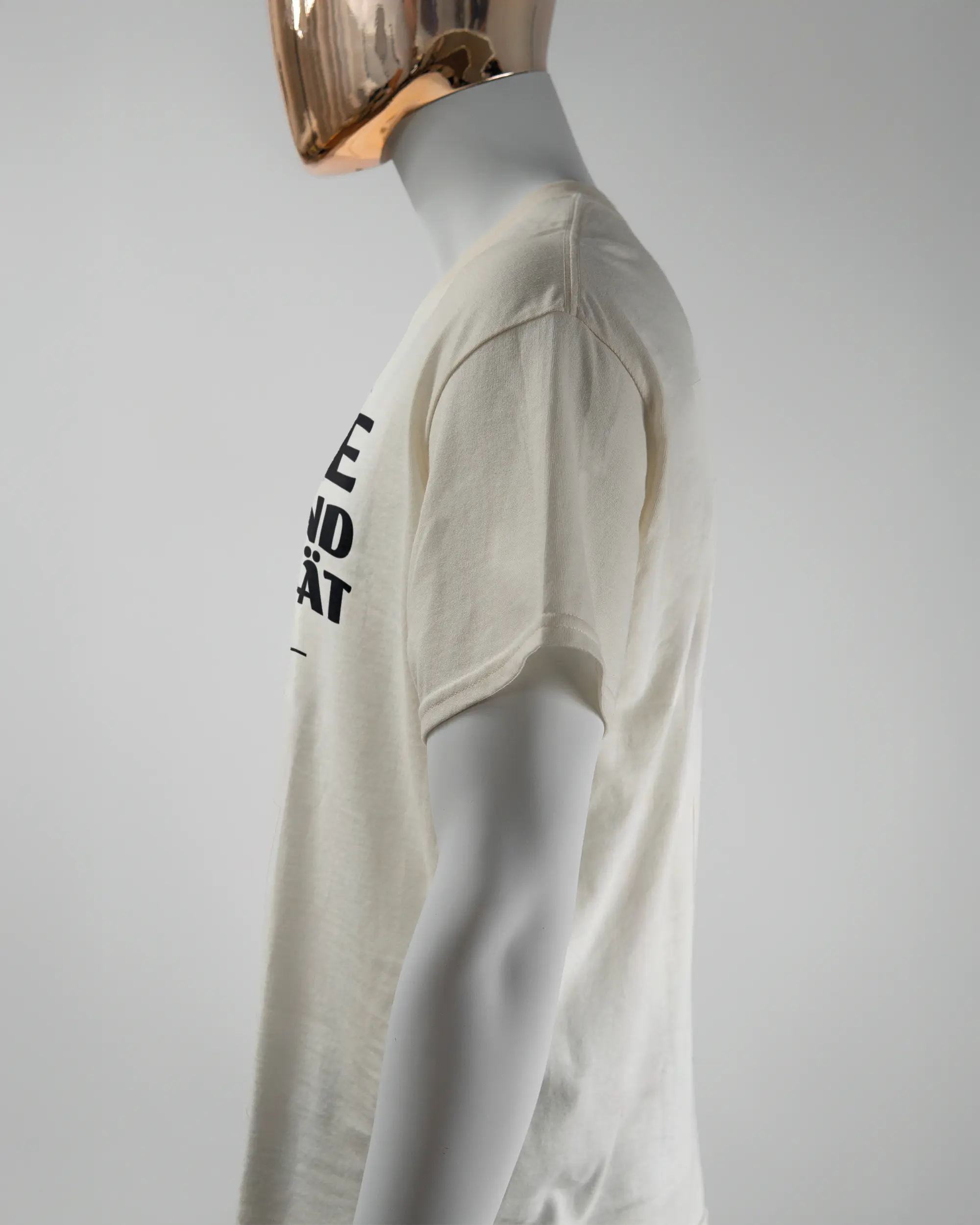 Seitenansicht des Basic Unisex T-Shirt Regular von Maondo mit dem Design Keine Eile vorne in der Farbe White und in der Größe L getragen von einer maskulinen Puppe