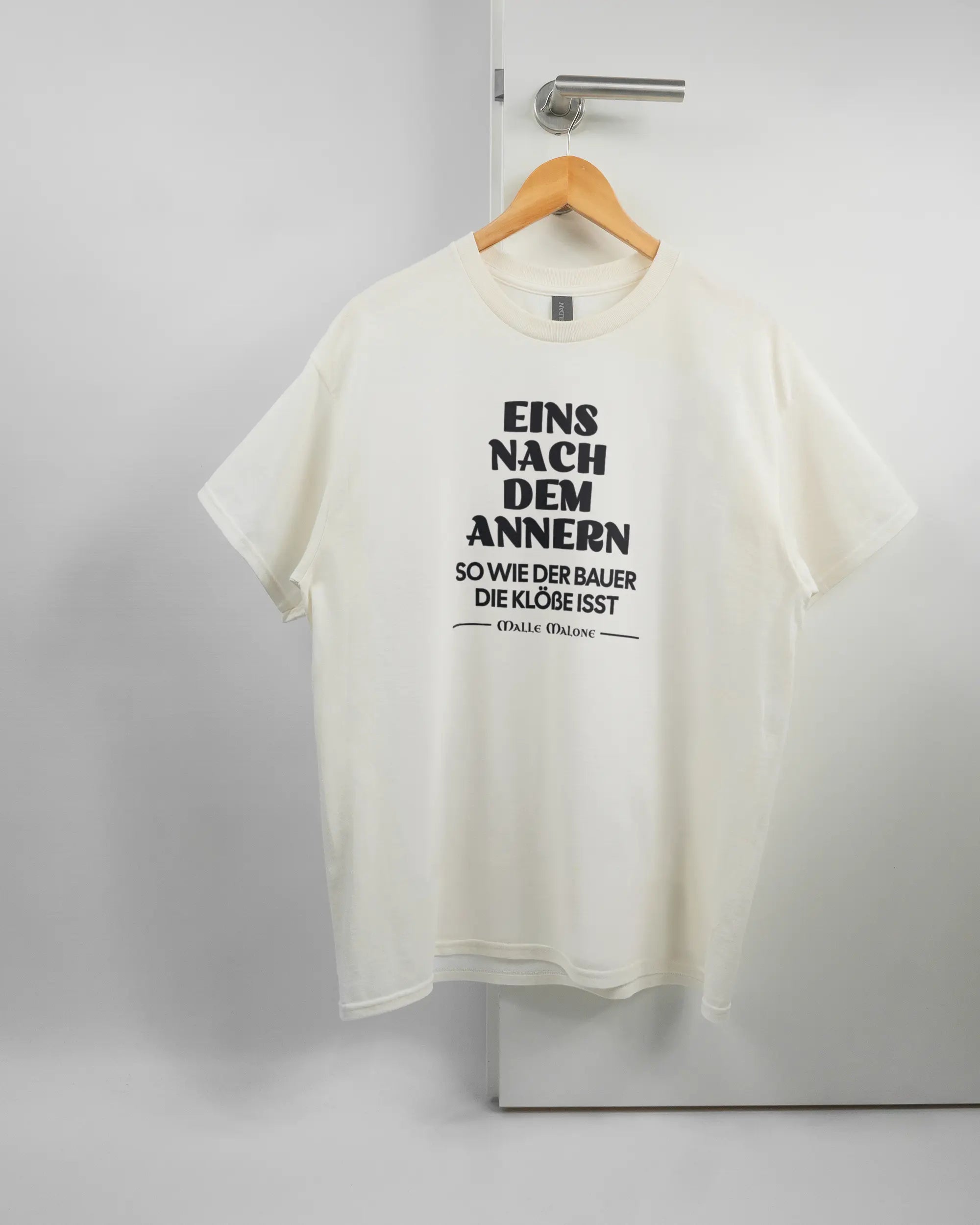 Vorderseite des Basic Unisex T-Shirt Regular von Maondo mit dem Design Eins nach dem Annern in der Farbe White und in der Größe L auf einem Bügel an der Türklinke aufgehängt
