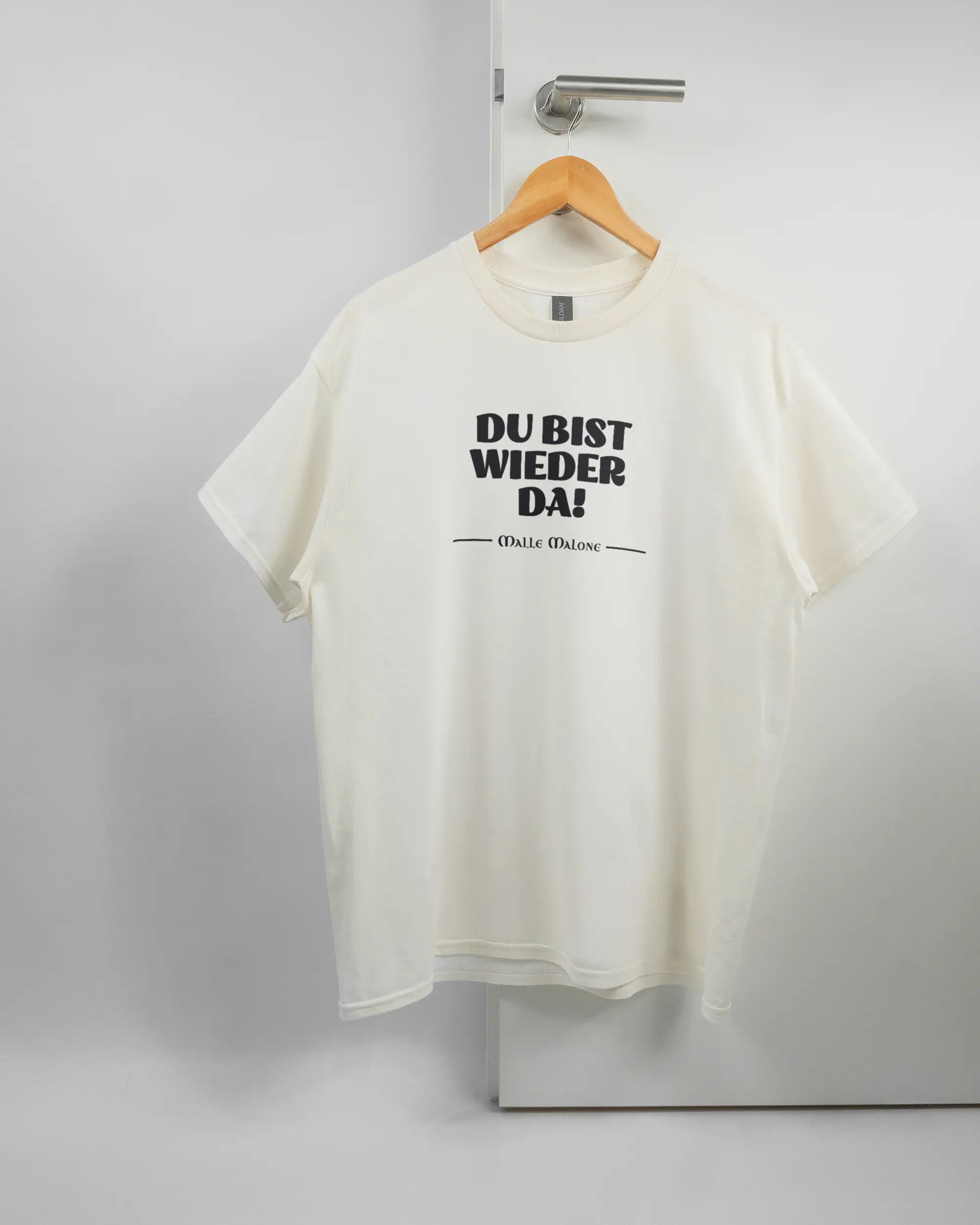 Vorderseite des Basic Unisex T-Shirt Regular von Maondo mit dem Design Wieder da in der Farbe White und in der Größe L auf einem Bügel an der Türklinke aufgehängt