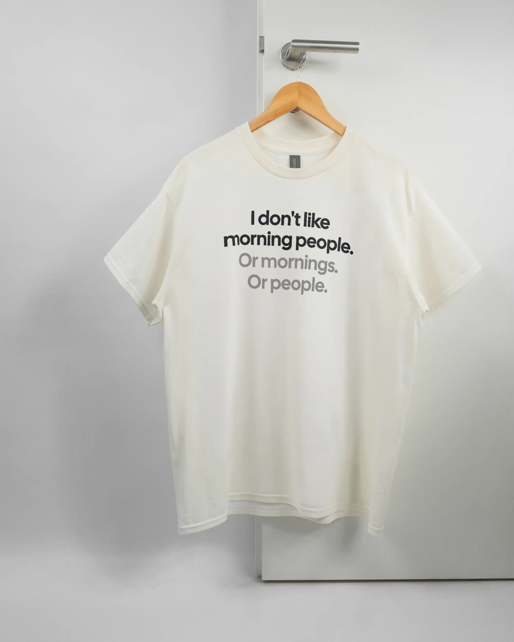 Vorderseite des Basic Unisex T-Shirt Regular von Maondo mit dem Design Morning Person in der Farbe White und in der Größe L auf einem Bügel an der Türklinke aufgehängt