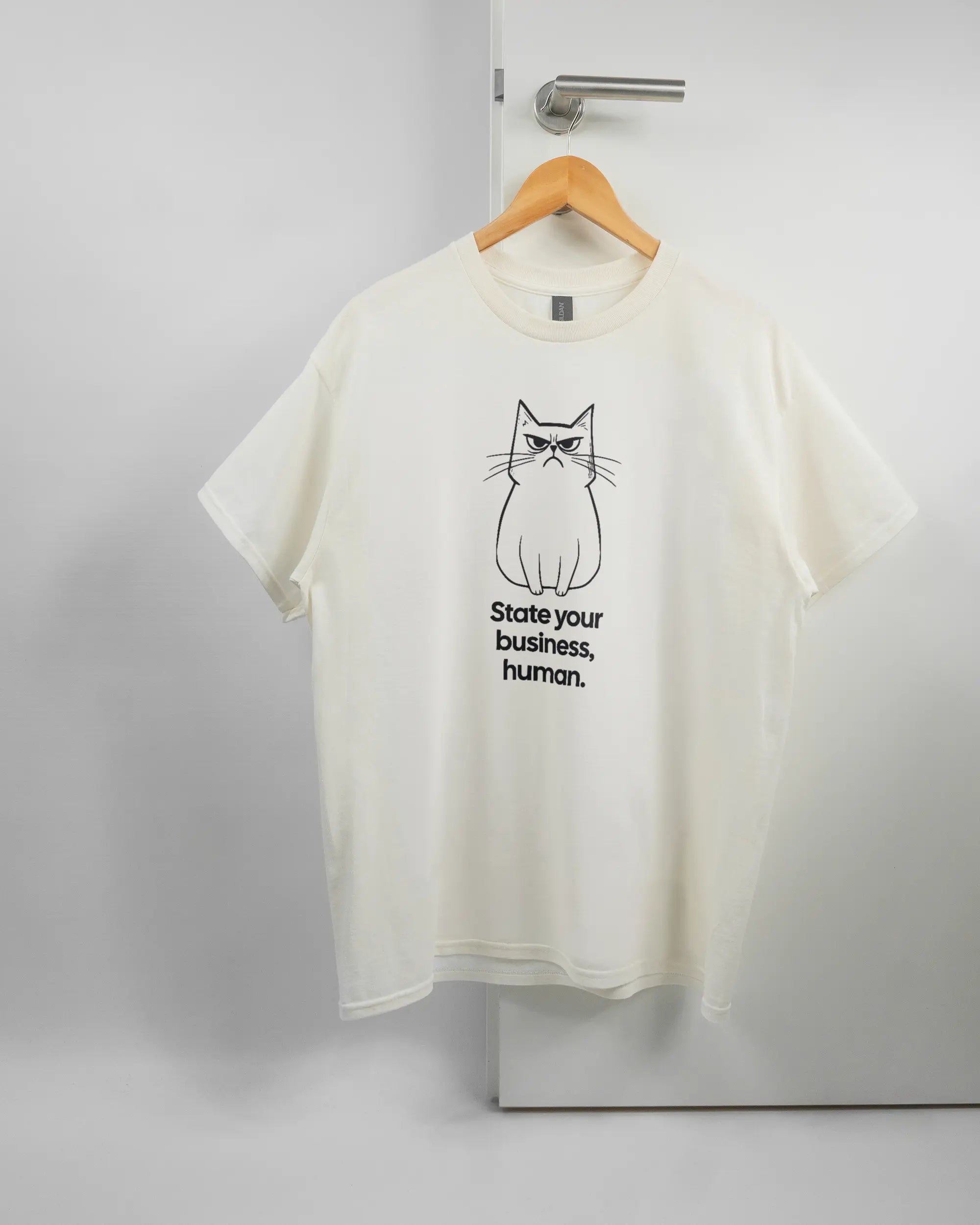Vorderseite des Basic Unisex T-Shirt Regular von Maondo mit dem Design Grumpy Purr in der Farbe White und in der Größe L auf einem Bügel an der Türklinke aufgehängt