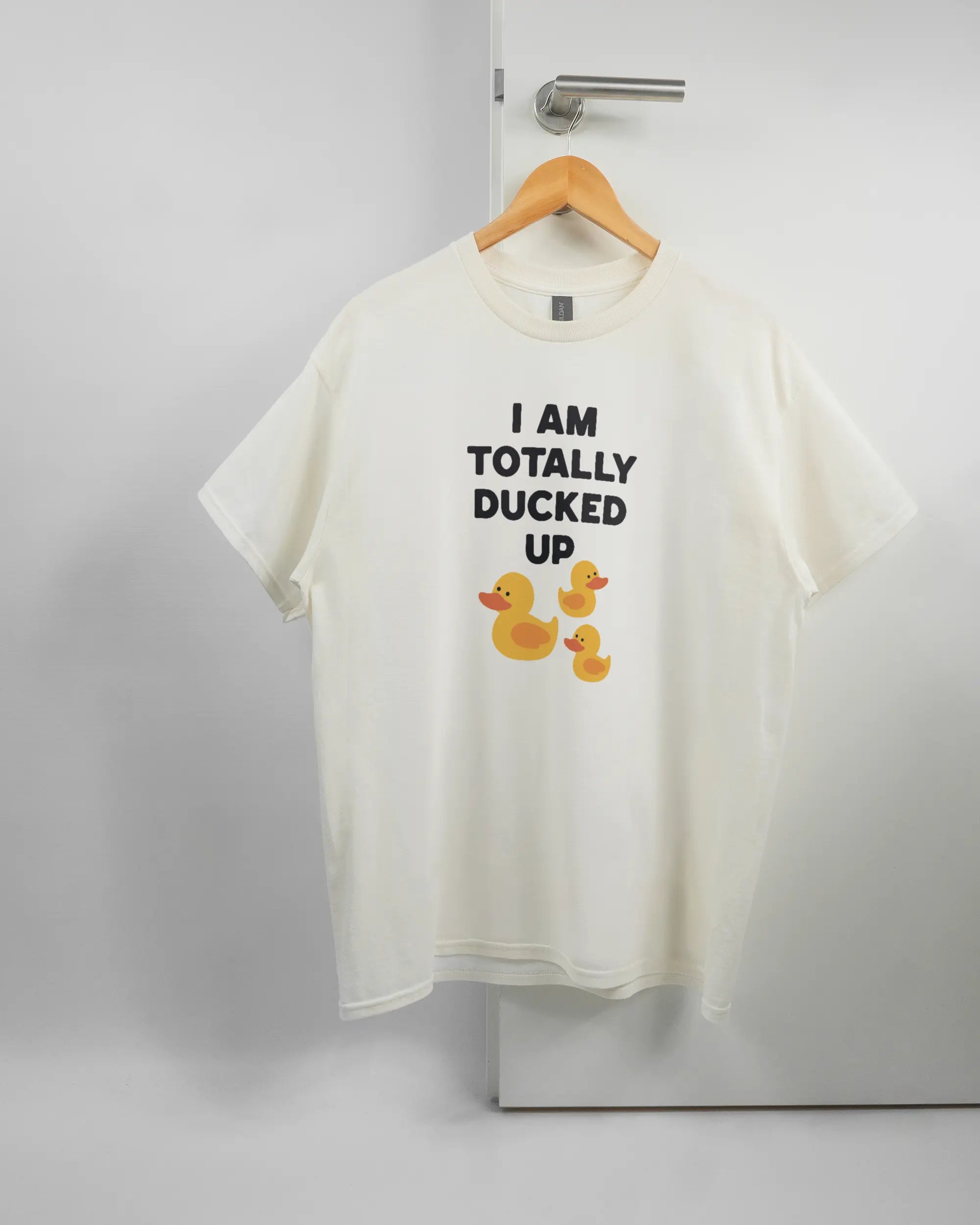 Vorderseite des Basic Unisex T-Shirt Regular von Maondo mit dem Design Ducked Up in der Farbe White und in der Größe L auf einem Bügel an der Türklinke aufgehängt