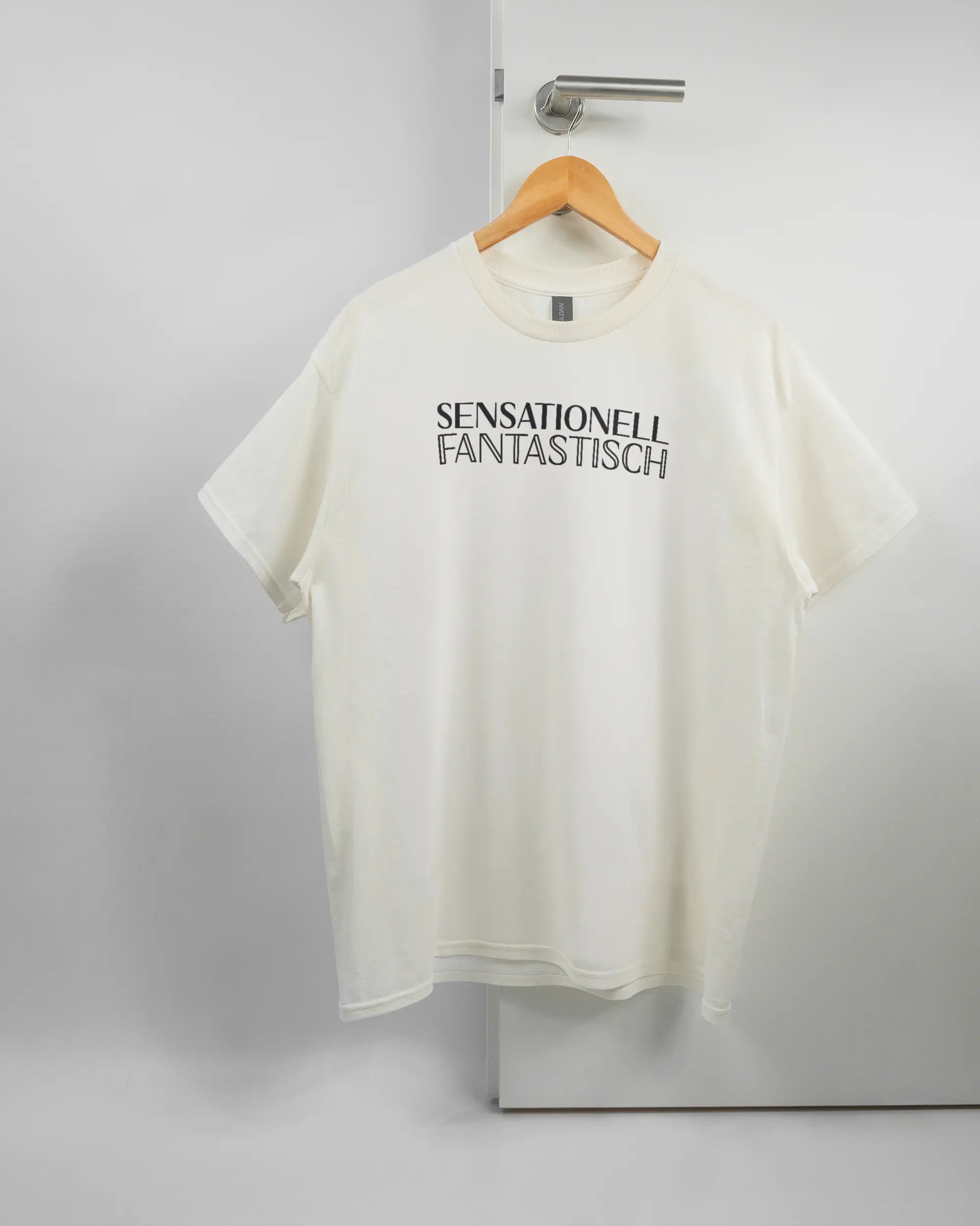 Vorderseite des Basic Unisex T-Shirt Regular von Maondo mit dem Design Sensationell in der Farbe White und in der Größe L auf einem Bügel an der Türklinke aufgehängt