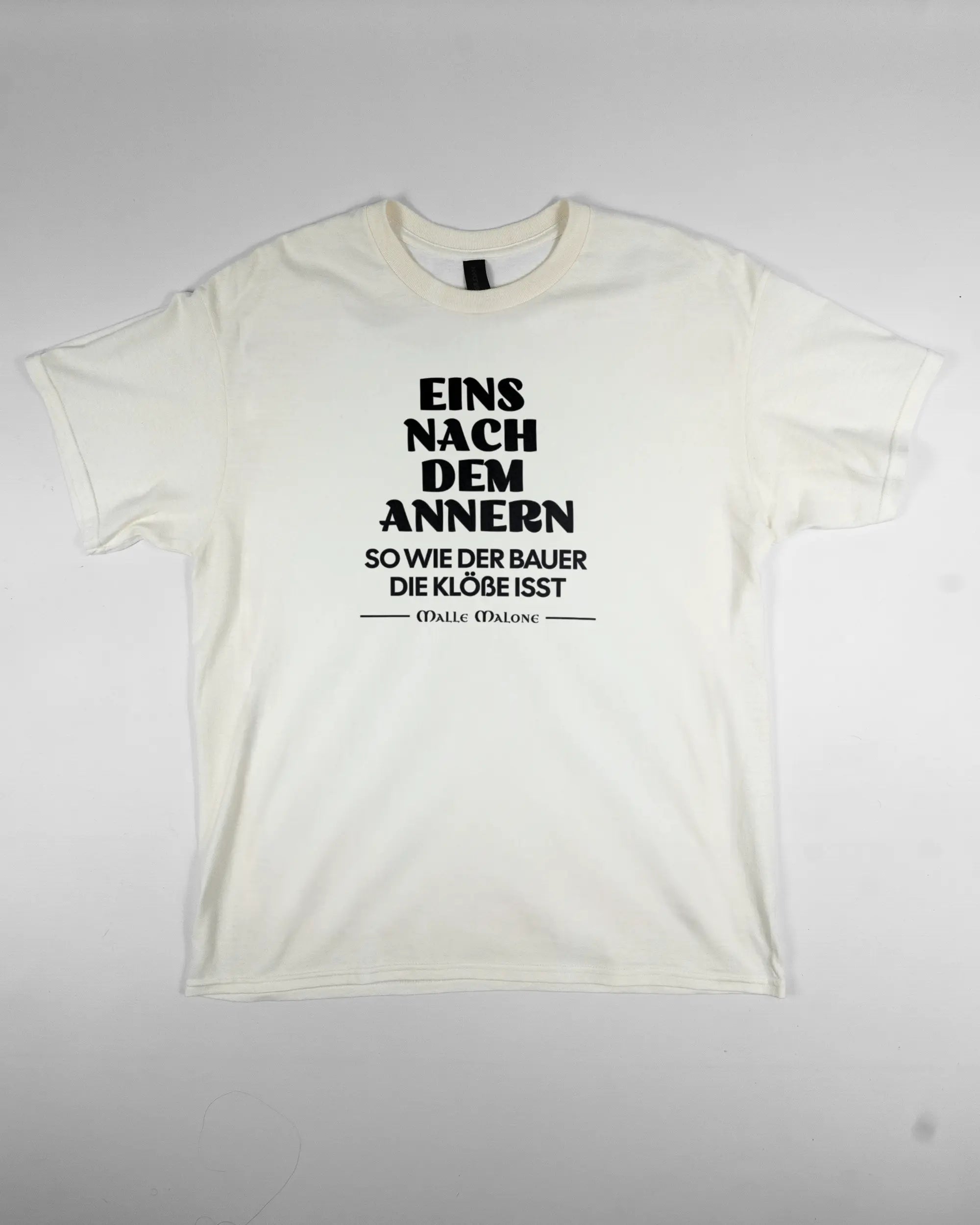 Vorderseite des Basic Unisex T-Shirt Regular von Maondo mit dem Design Eins nach dem Annern in der Farbe White und in der Größe L flach auf den Boden gelegt