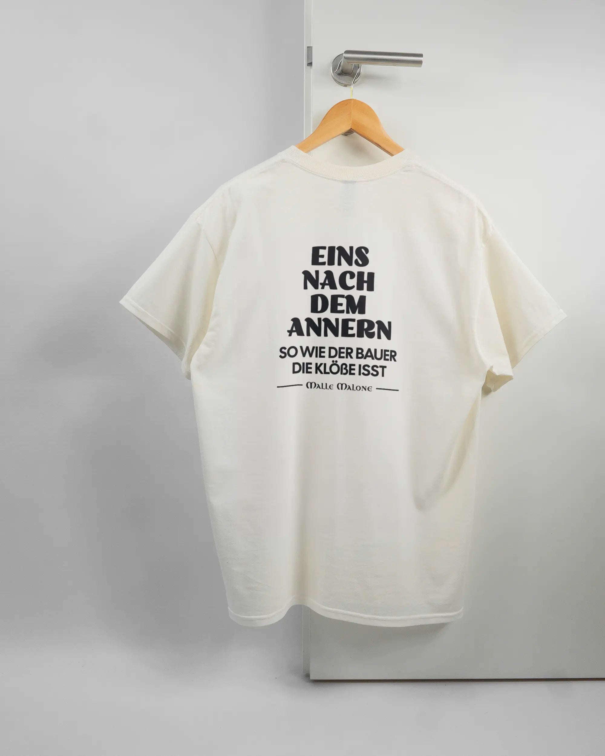 Rückseite des Basic Unisex T-Shirt Regular von Maondo mit dem Design Eins nach dem Annern in der Farbe White und in der Größe L auf einem Bügel an der Türklinke aufgehängt