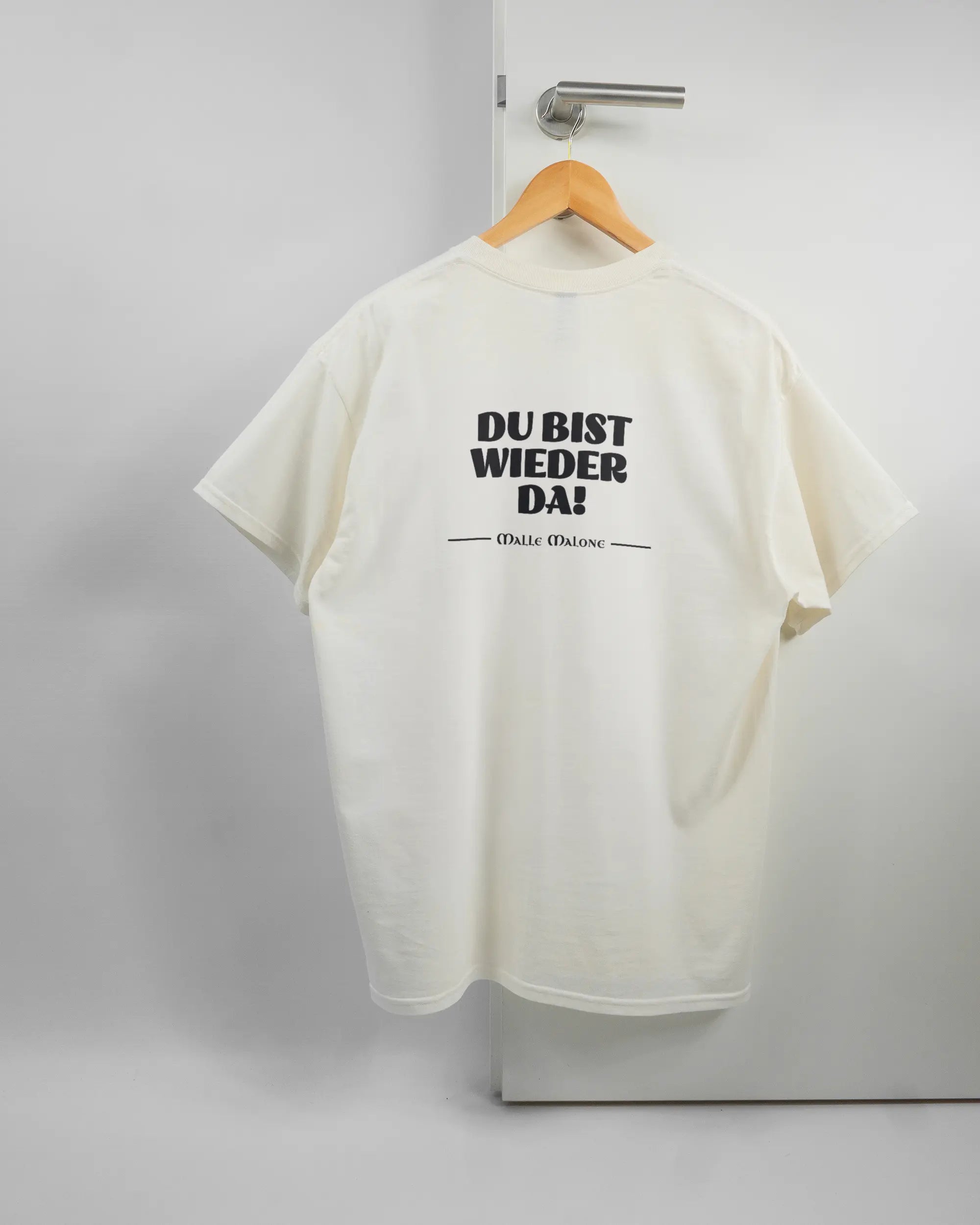 Rückseite des Basic Unisex T-Shirt Regular von Maondo mit dem Design Wieder da in der Farbe White und in der Größe L auf einem Bügel an der Türklinke aufgehängt