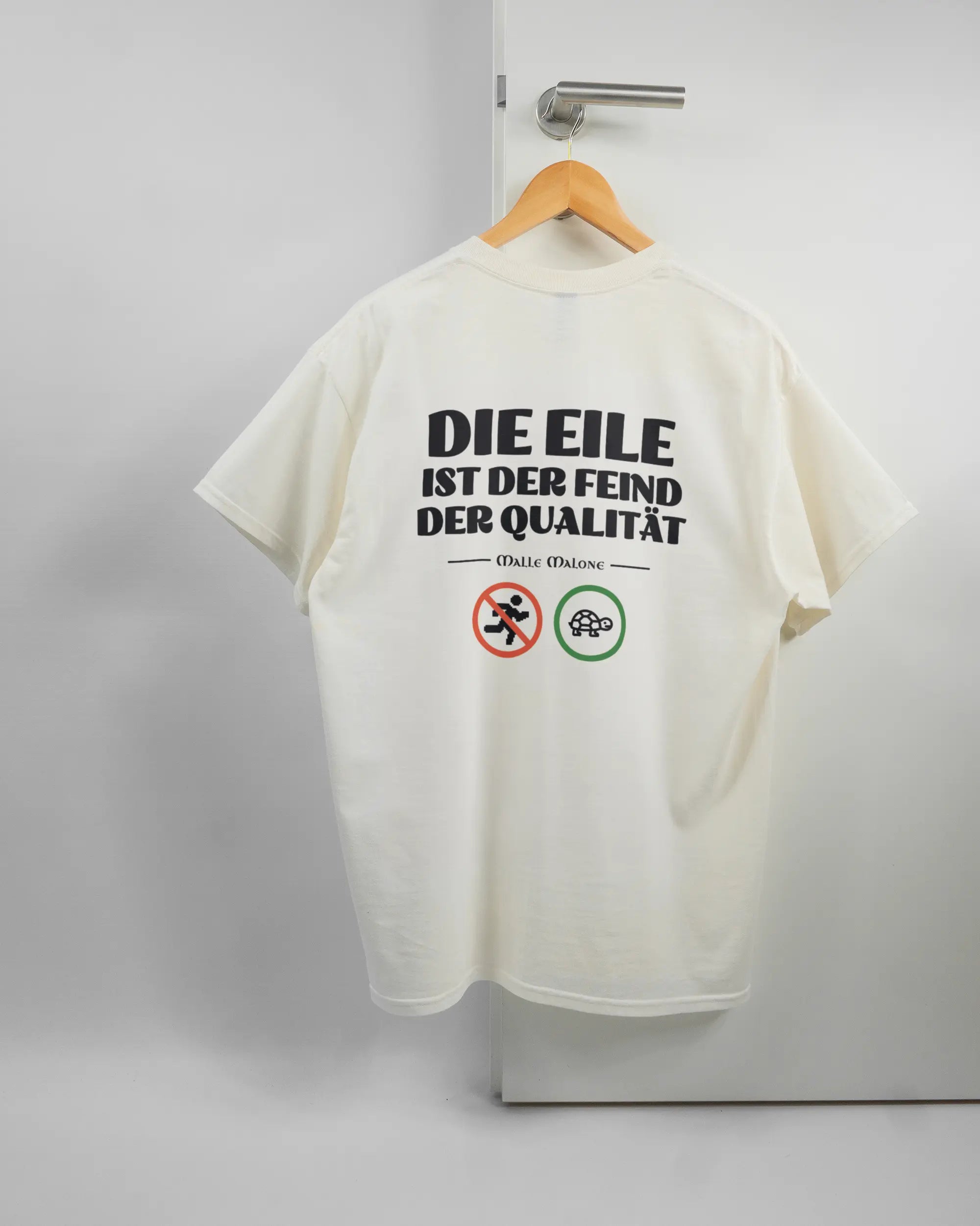 Rückseite des Basic Unisex T-Shirt Regular von Maondo mit dem Design Keine Eile in der Farbe White und in der Größe L auf einem Bügel an der Türklinke aufgehängt
