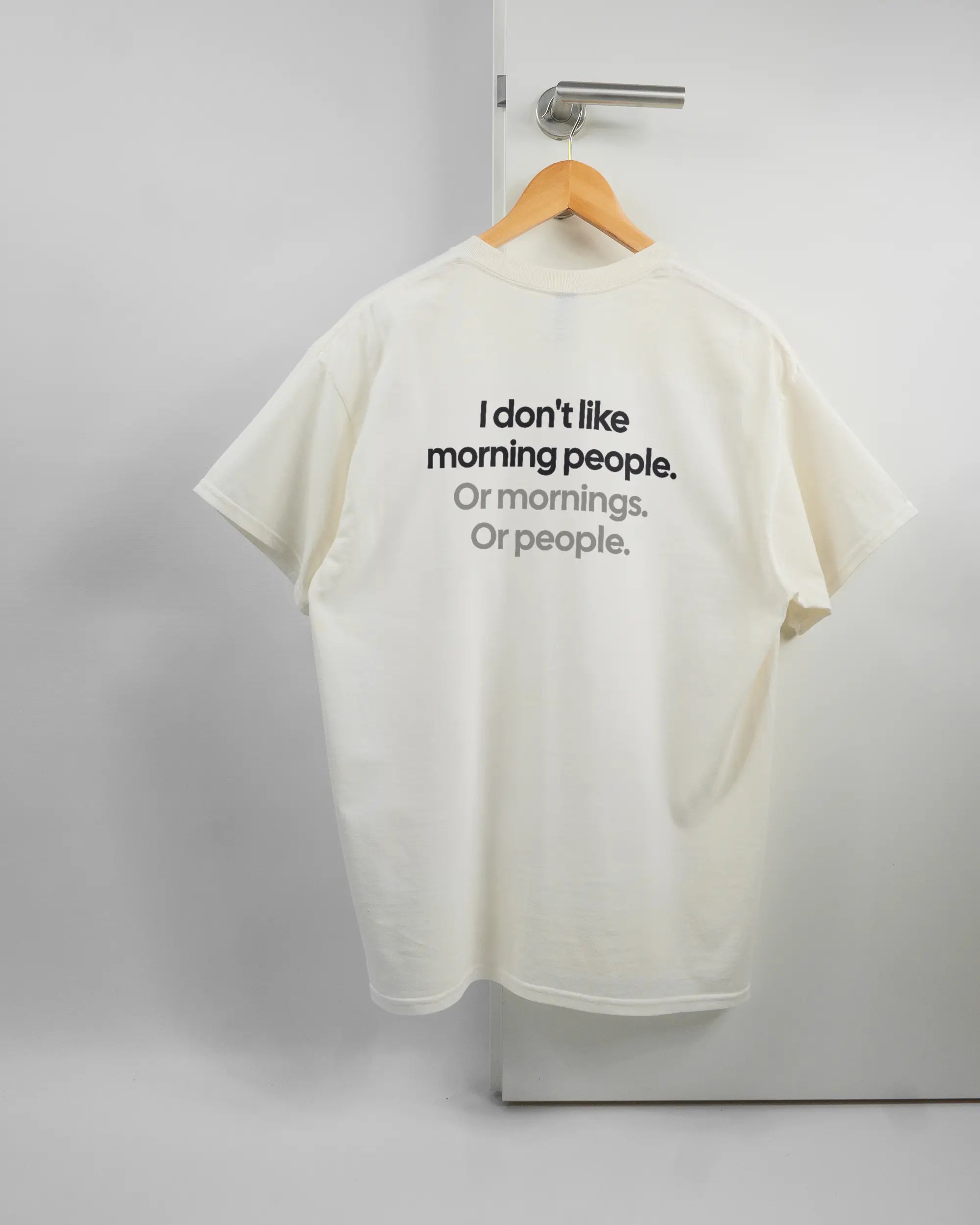 Rückseite des Basic Unisex T-Shirt Regular von Maondo mit dem Design Morning Person in der Farbe White und in der Größe L auf einem Bügel an der Türklinke aufgehängt