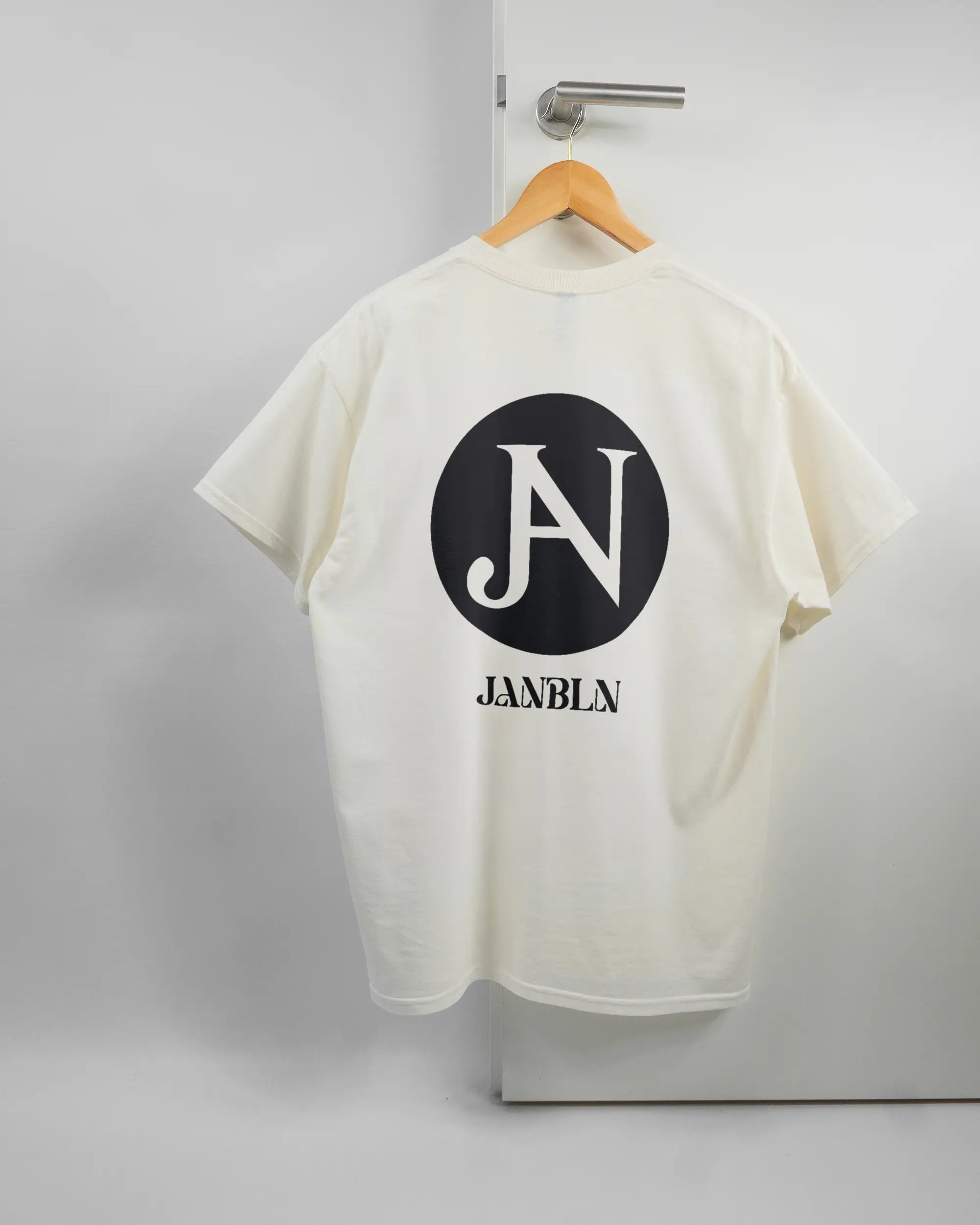 Rückseite des Basic Unisex T-Shirt Regular von Maondo mit dem Design JB1 in der Farbe White und in der Größe L auf einem Bügel an der Türklinke aufgehängt