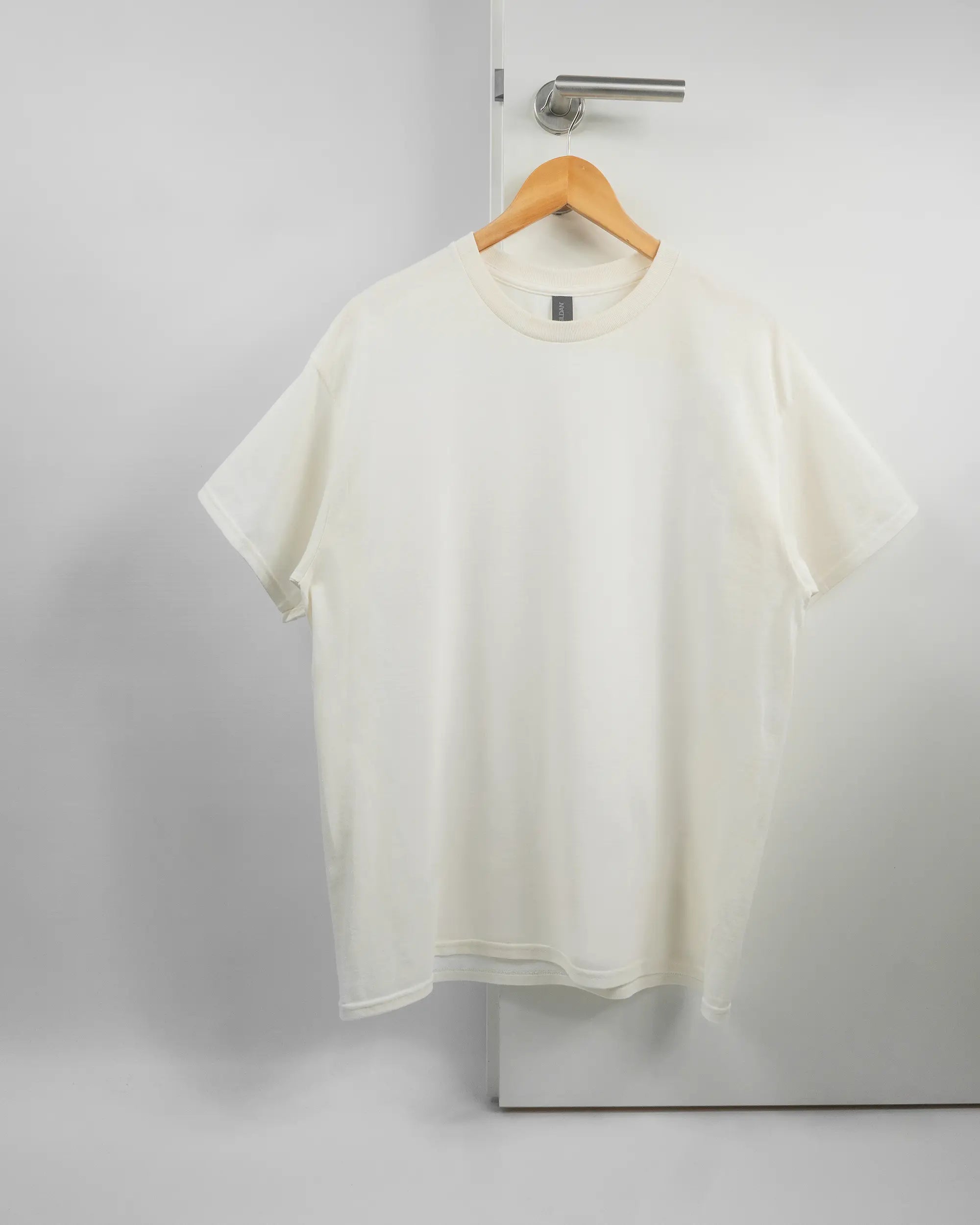 Vorderseite des Basic Unisex T-Shirt Regular von Maondo ohne Motiv in der Farbe White und in der Größe L auf einem Bügel an der Türklinke aufgehängt
