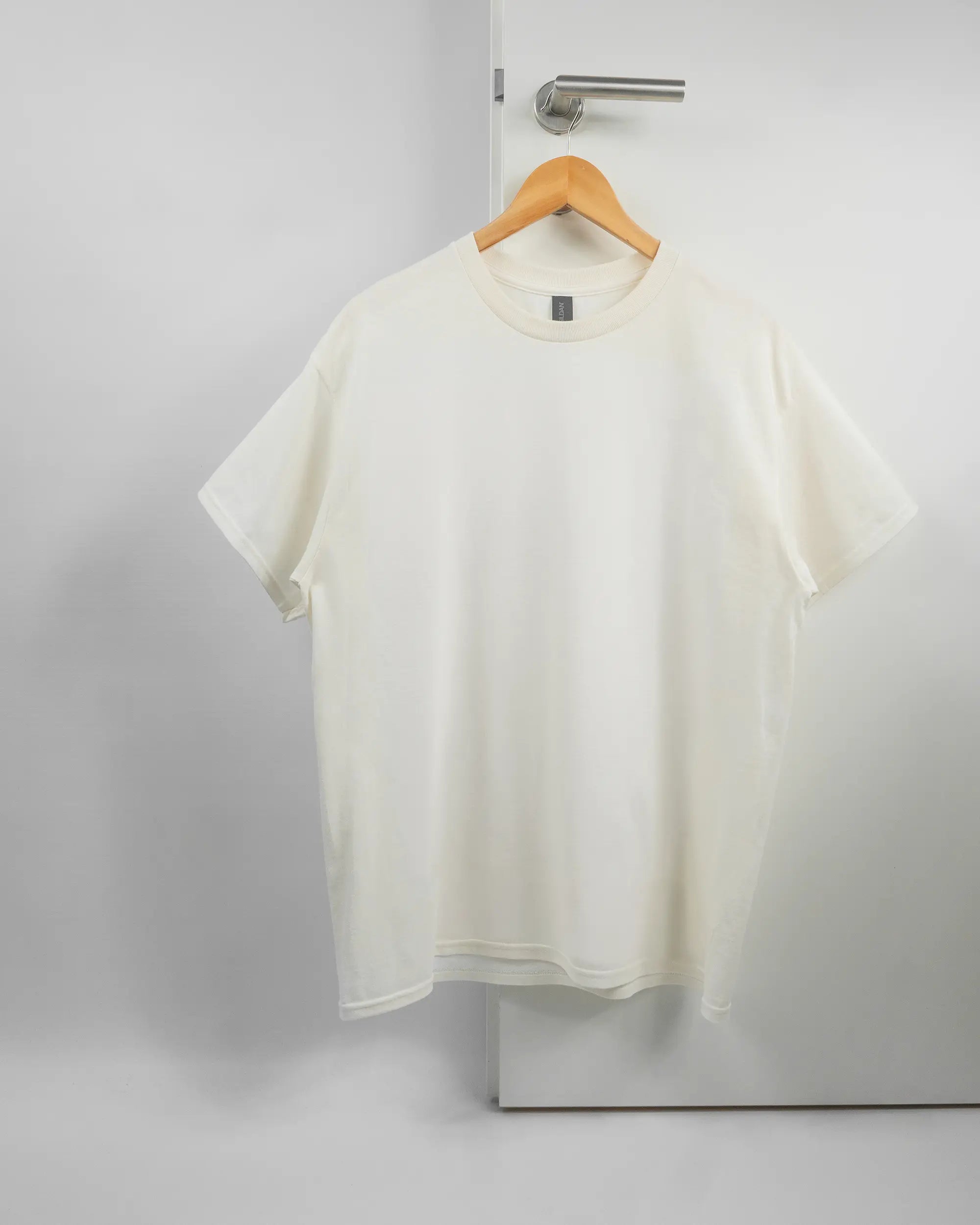 Vorderseite des Basic Unisex T-Shirt Regular von Maondo ohne Motiv in der Farbe White und in der Größe L auf einem Bügel an der Türklinke aufgehängt